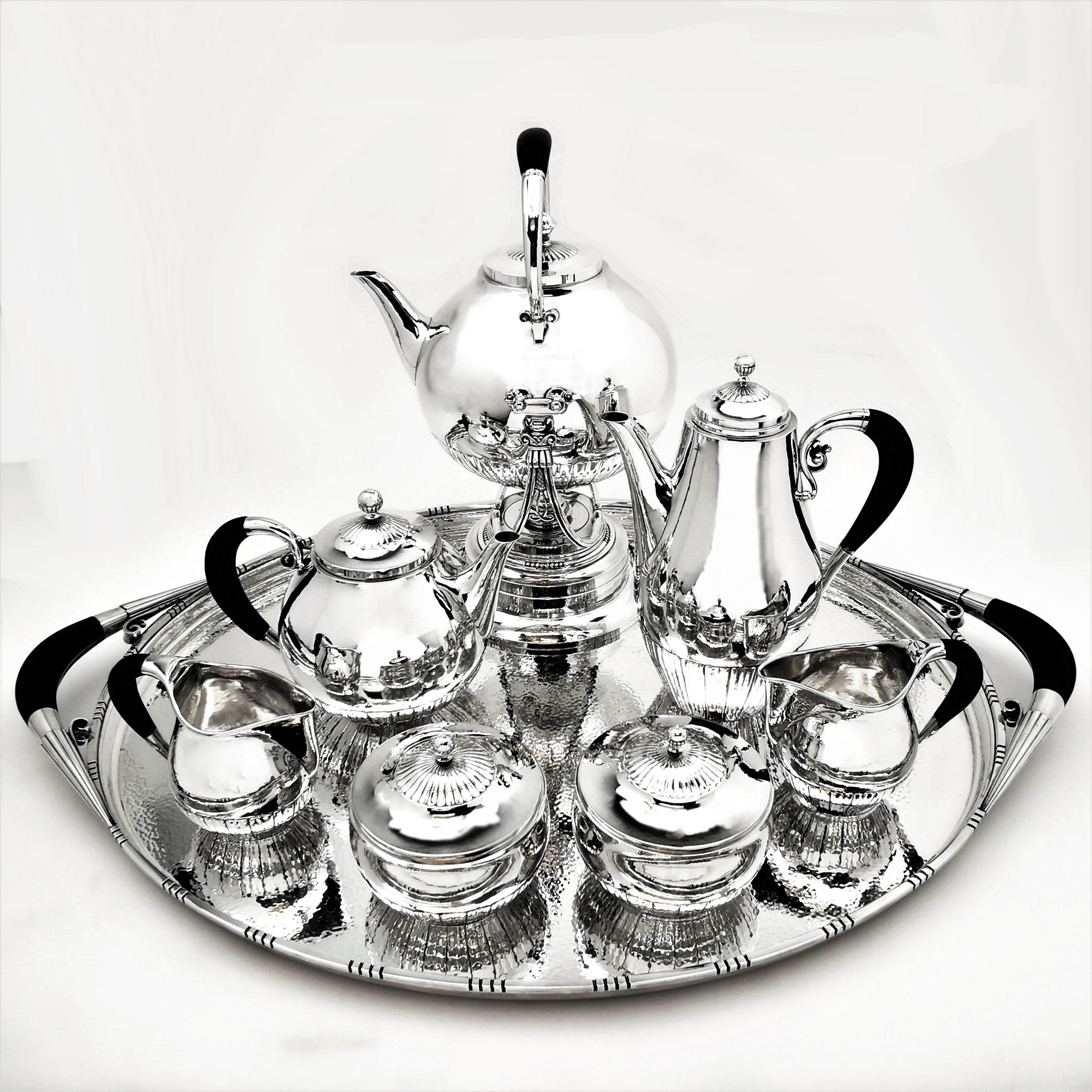 A magnificent Danish Georg Jensen 8 piece Tea and Coffee set in the Cosmos Pattern. The set comprises of a Kettle on Stand, Coffee Pot, Tea Pot, two Milk / Cream Jugs and two lidded Sugar Bowls on large Tea Tray.
The handles of the set are a shaped