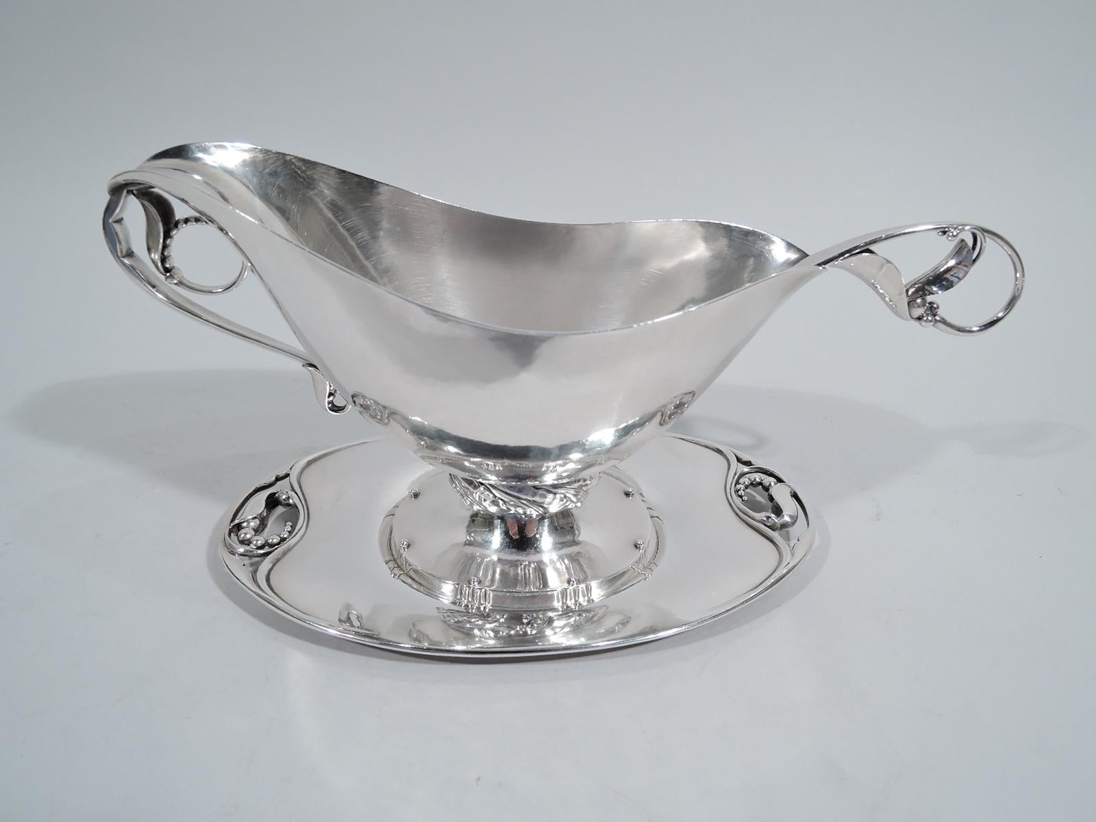 Art nouveau hand-hammered sterling silver gravy boat on stand. Made by Georg Jensen in Denmark. Boat with lip spout, thumb rest and scroll hand with rinceaux-style seed-and-leaf finger ring. Tooled and tubular support on raised oval foot with tooled