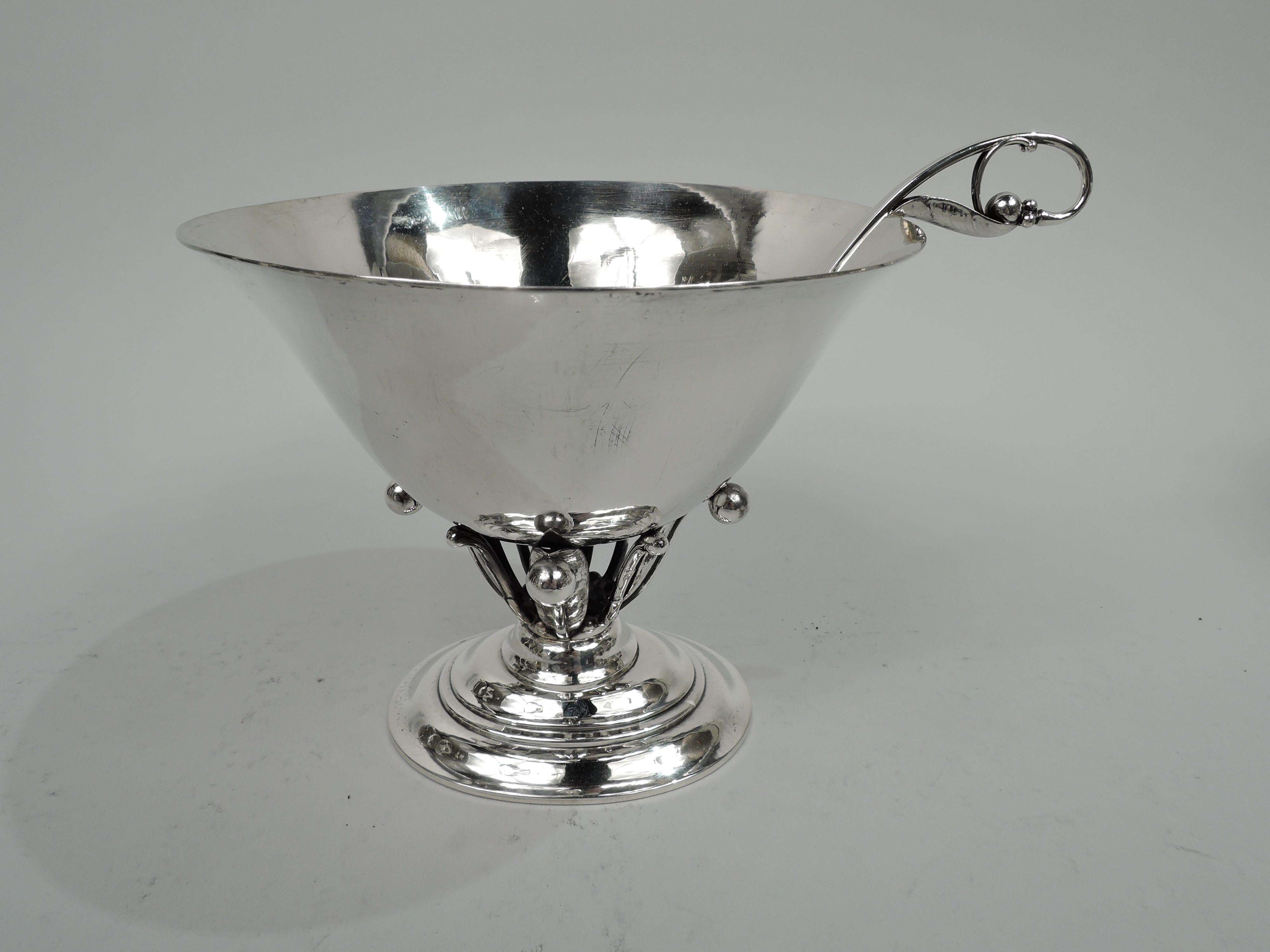 Moderna composta in argento sterling. Prodotto da Georg Jensen in Danimarca. Ciotola conica con bordo svasato su supporto aperto con foglie stilizzate, viticci e perline, montata su piede ovale a gradini. Martellamento a mano visibile. Completamente