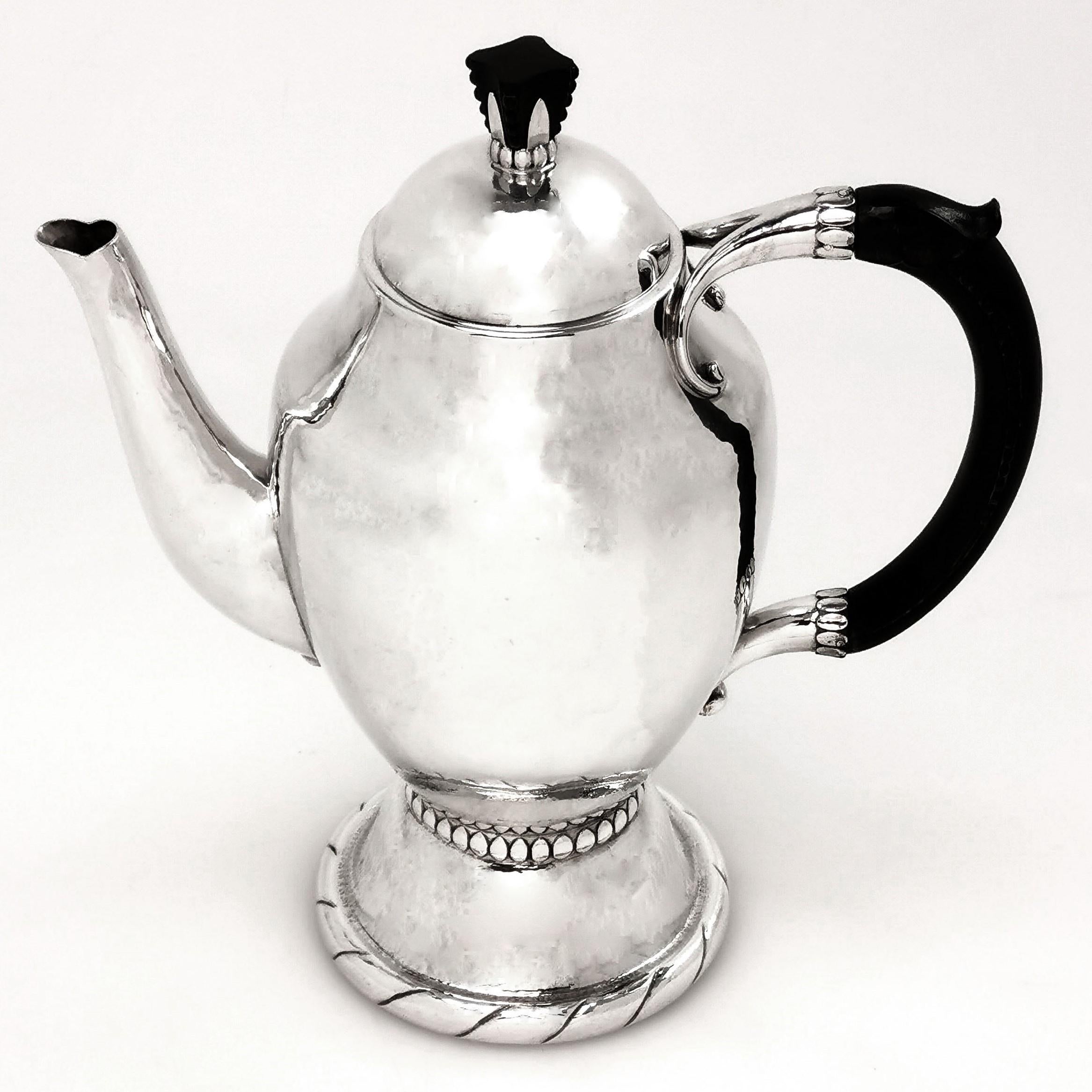 An impressive Arts & Crafts solid silver Coffee Pot by Danish Silversmith Georg Jensen. This coffee pot stands on a tall spread foot and has a wooden handle and finial. The Coffee Pot has a lightly hammered finish.

This Coffee Pot is made in