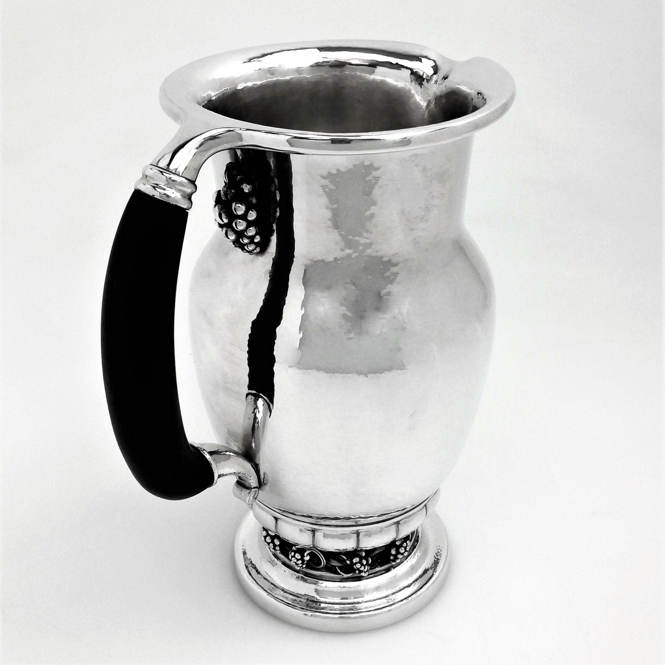 A magnificent sterling Silver Georg Jensen Jug with a wooden handle and embellished with a grape and vine motif. The Pitcher has a bunch of grapes below the handle on the upper lip and a band of grapes applied above the spread foot. The exterior of