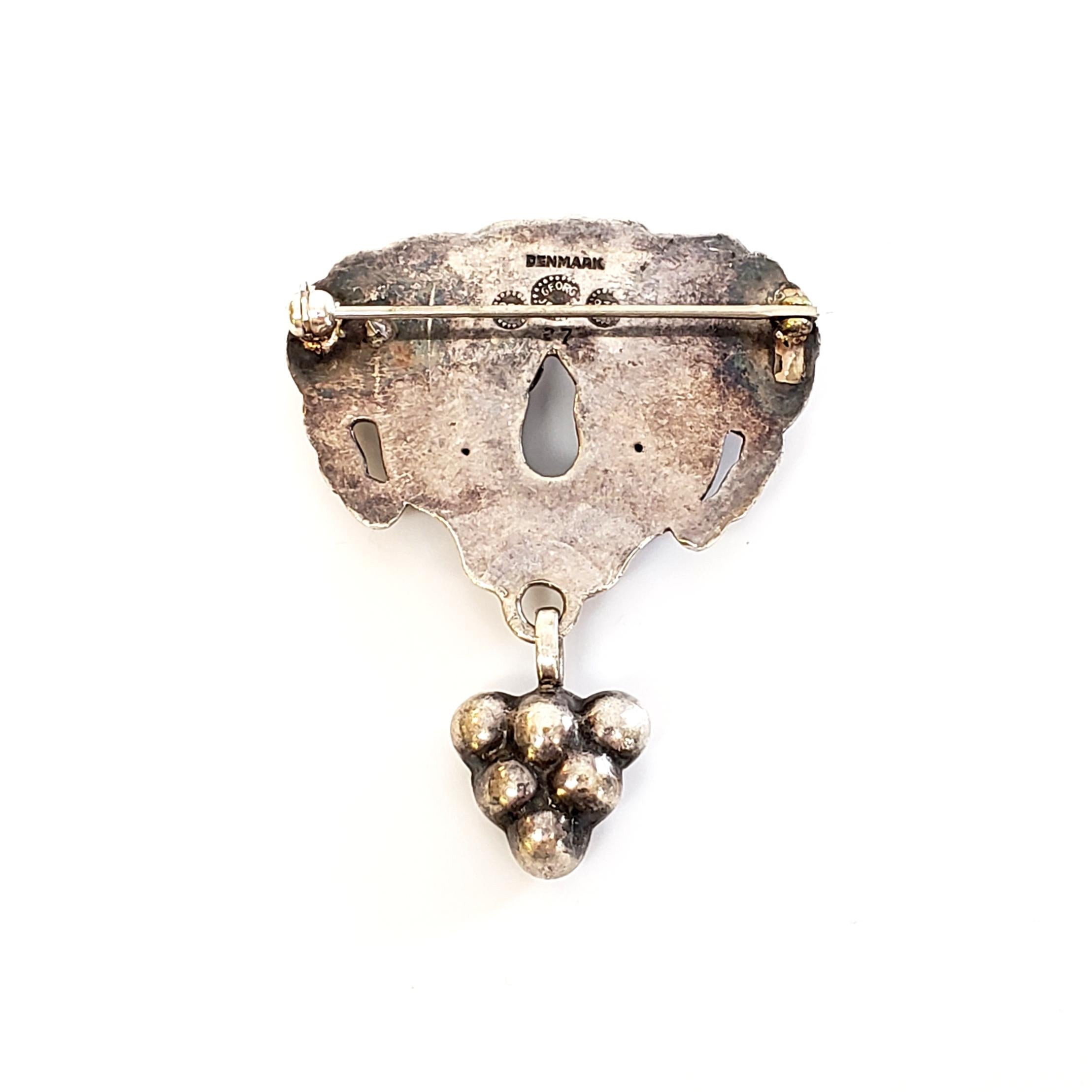 Vintage Georg Jensen 830 silver and glass brooch/pin, #27, circa 1915-1927.

This brooch is typical of Georg Jensen pieces in that it is inspired by nature motifs. This highly collectible brooch features dangling grape cluster from a leaf/swag