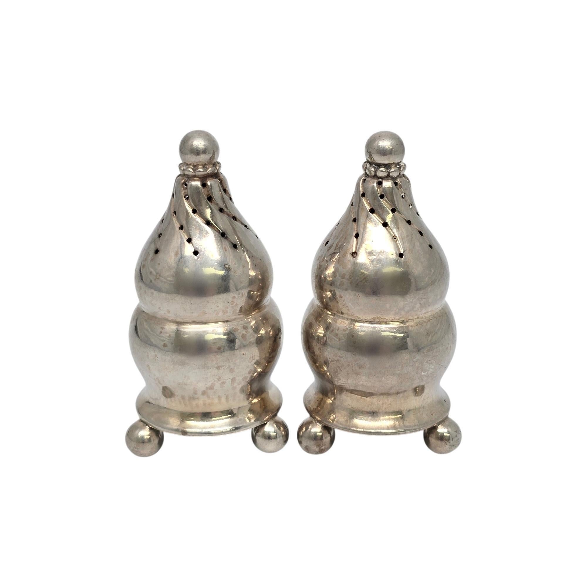 Vintage Georg Jensen Denmark sterling silver salt and pepper shakers with monogram, pattern #410.

Monogram appears to be H on the bottom of each shaker.

These shakers are bulbus in shape atop 3 ball feet, with a twist design at top. Hallmarks date