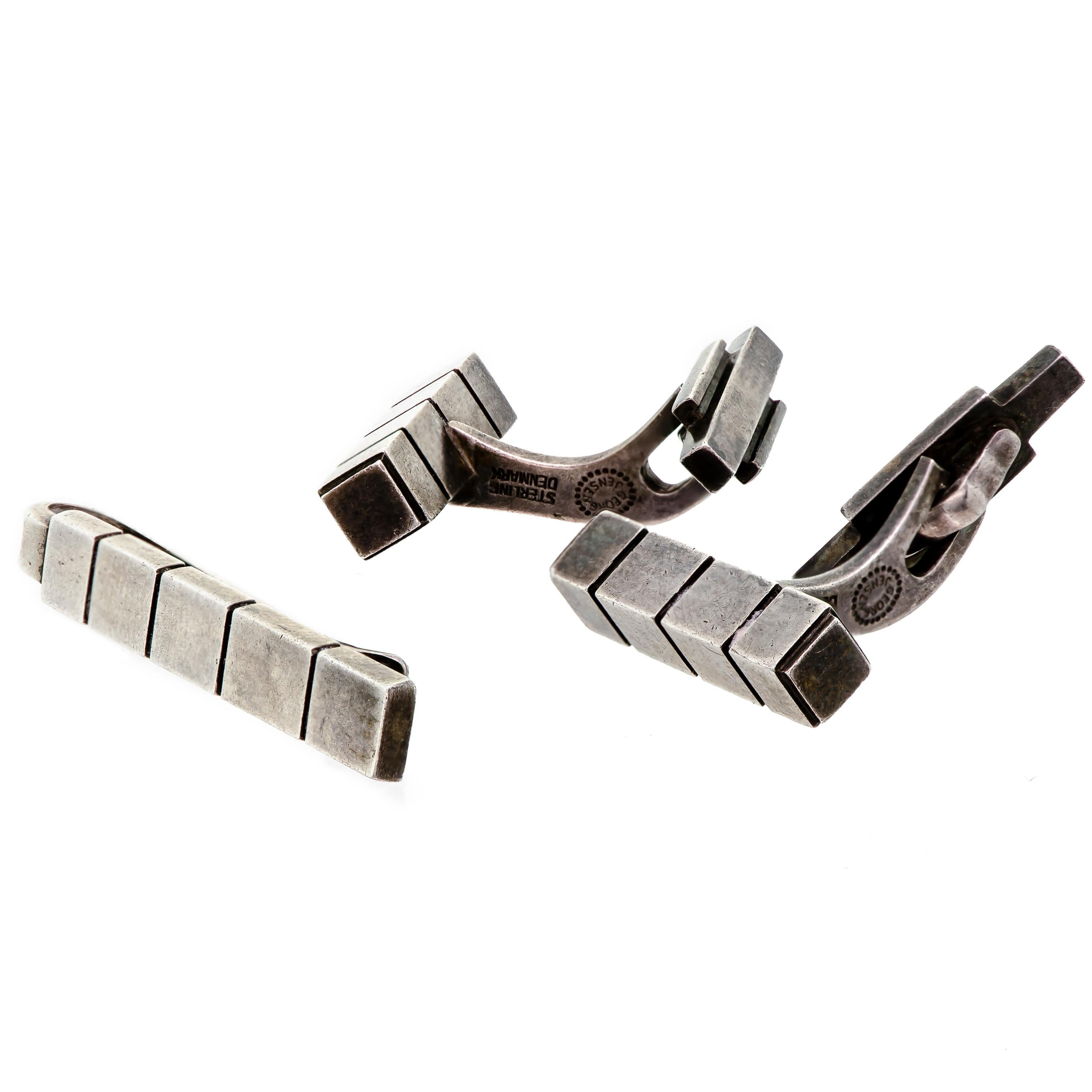 Indulge in the sophisticated charm of the Georg Jensen Mid-Century Cufflinks and Tie Bar Set, a meticulously crafted accessory from the 1960s. This set boasts a striking mid-century design that exudes elegance and refinement. Its sterling silver