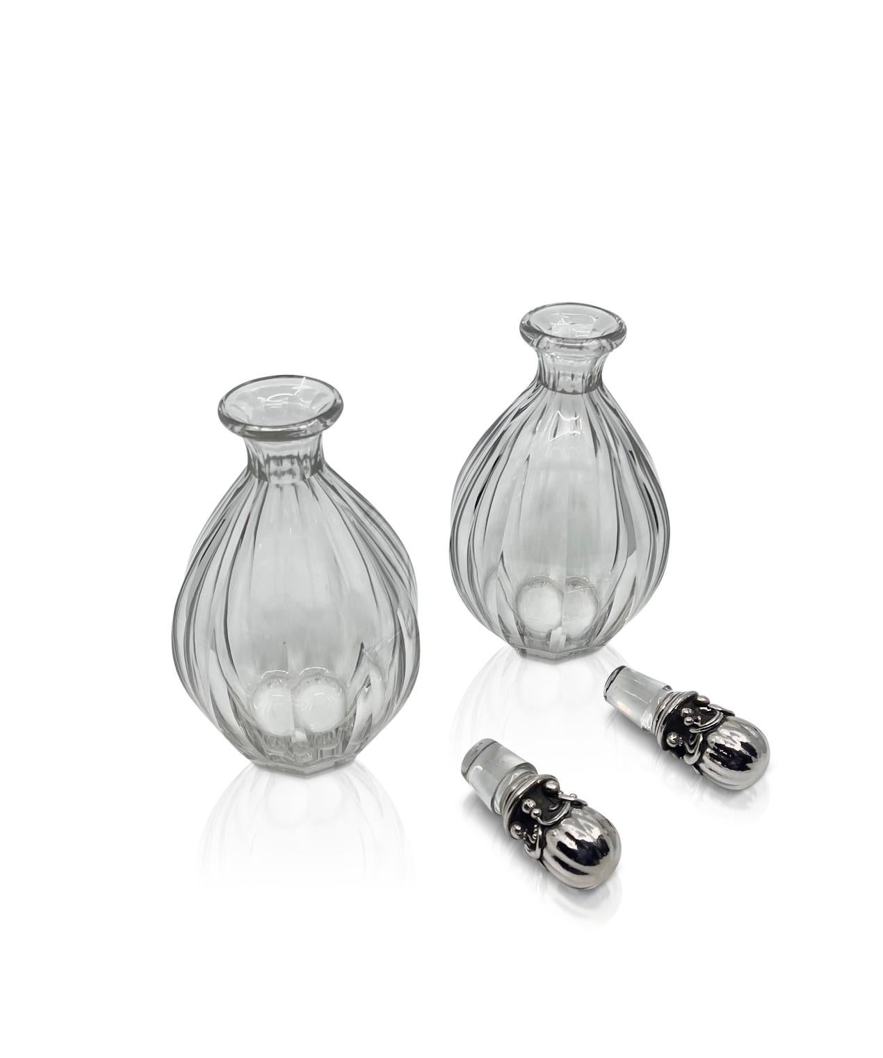 A matching pair of vintage Georg Jensen sterling silver ornate stoppers #100 by Georg Jensen and Baccarat crystal decanters. The heavy art nouveau stoppers are hand crafted with a great deal of hand chasing involved. Each hand hammered stopper with