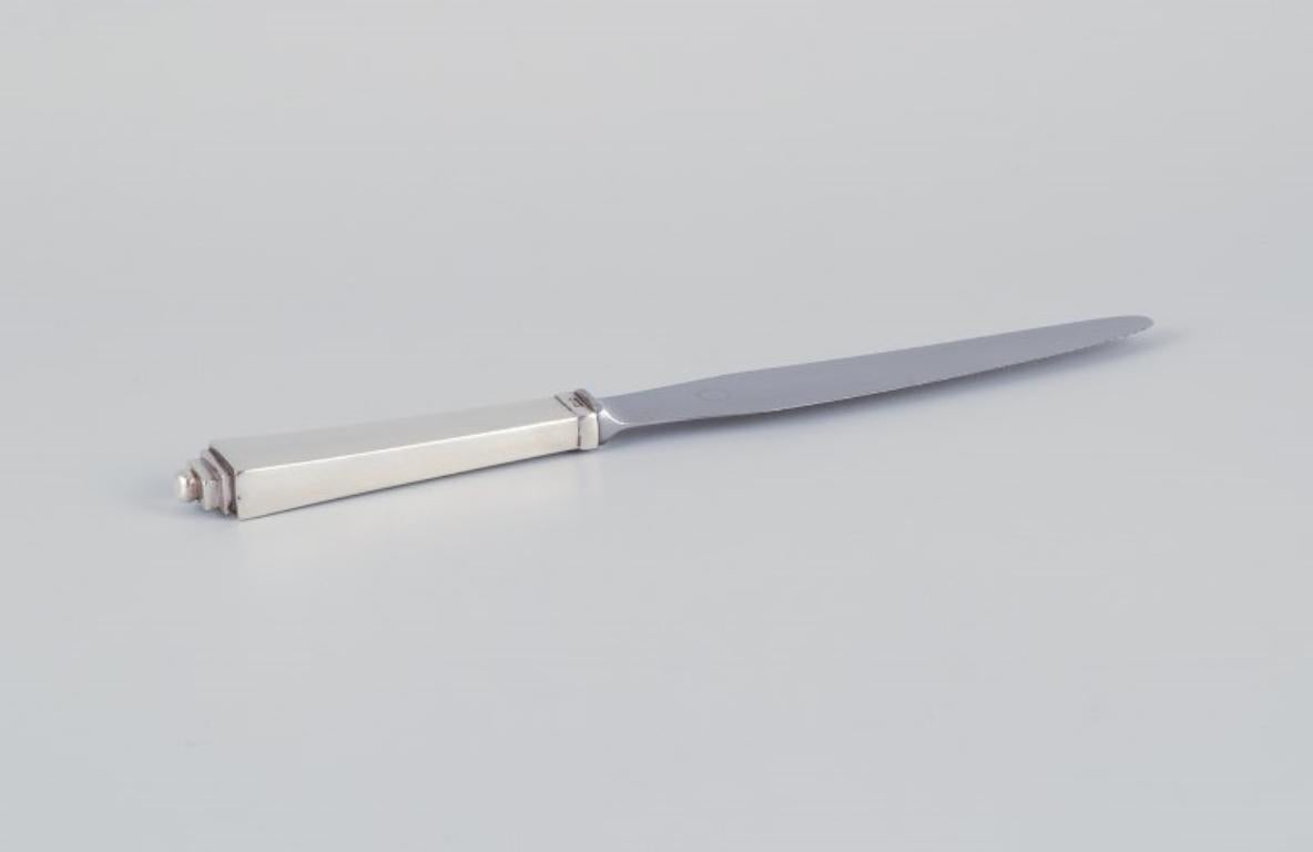 Georg Jensen Pyramide. 
Couteau de table Art Deco avec un long manche, une lame en acier inoxydable et un bord dentelé.
1933-1944 Poinçon.
En parfait état.
Dimensions : Longueur 24,0 cm.