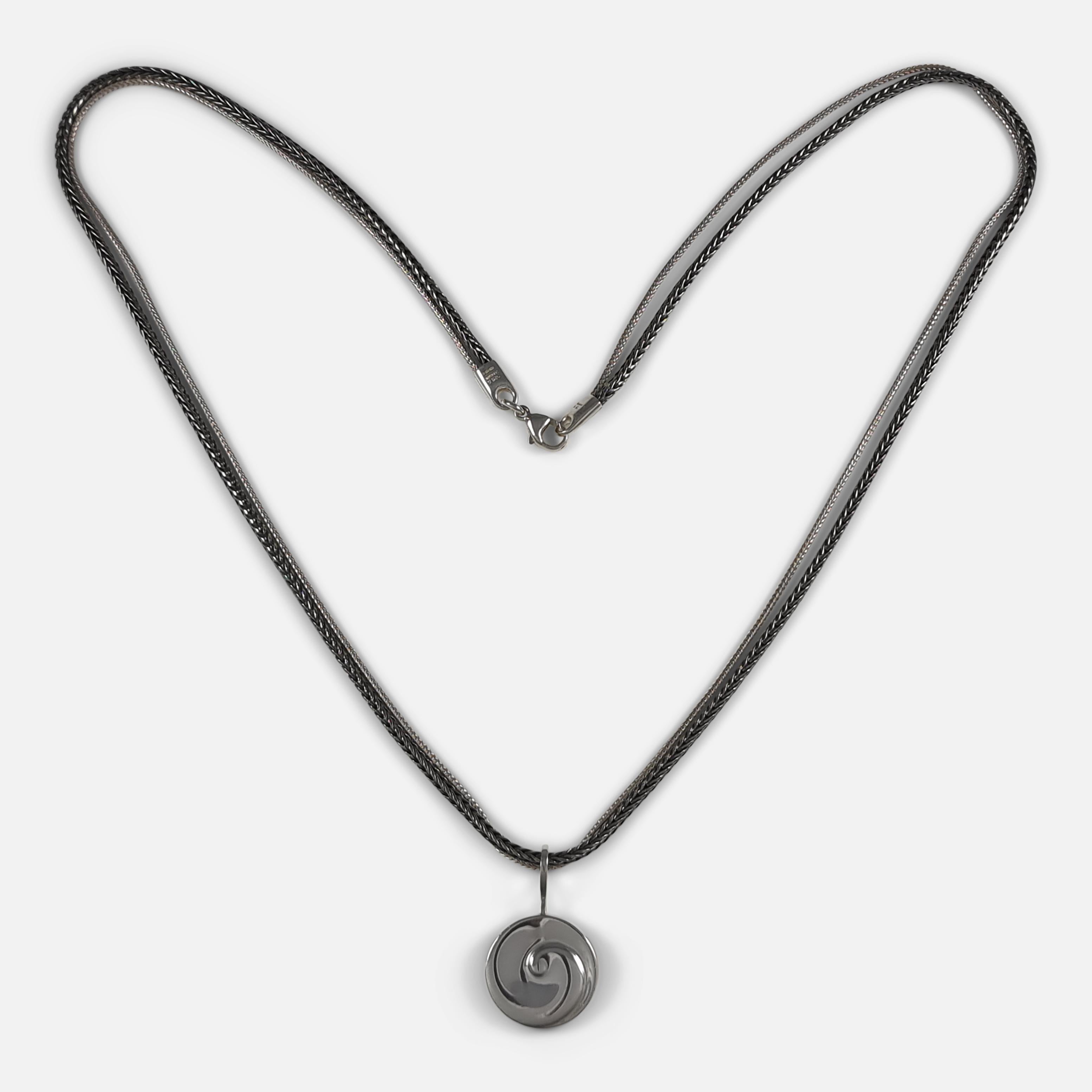 A sterling silver pendant #207, designed by Vivianna Torun Bülow-Hübe for Georg Jensen, with double strand chain. The pendant has a swirl effect to the front, on a double strand silver chain, with one strand being oxidised. 

The pendant is stamped