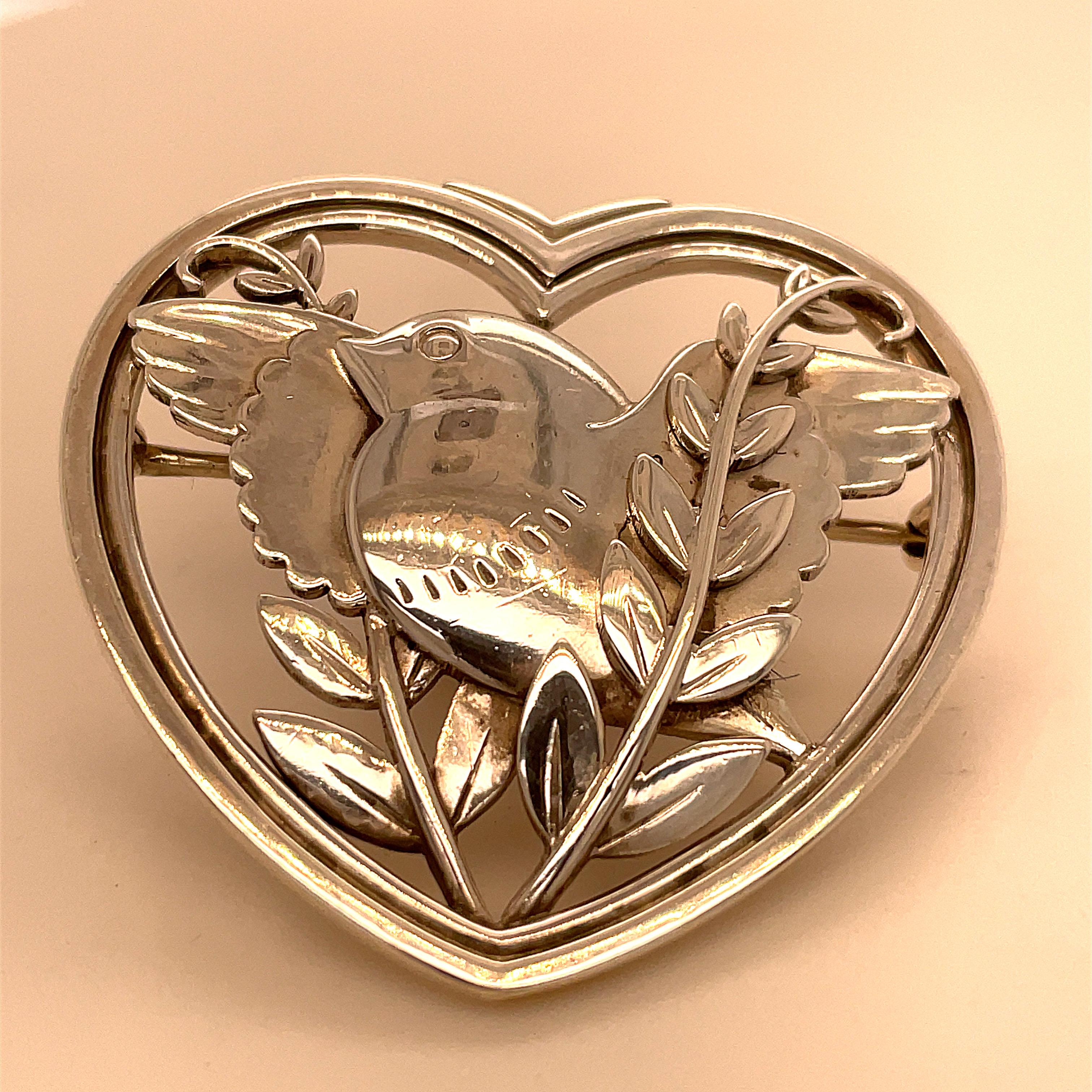 Large double-border figural heart pin.  Made and signed by Georg Jensen. Openwork center with an applied bird, sitting on a leafy branch.  1 3/4