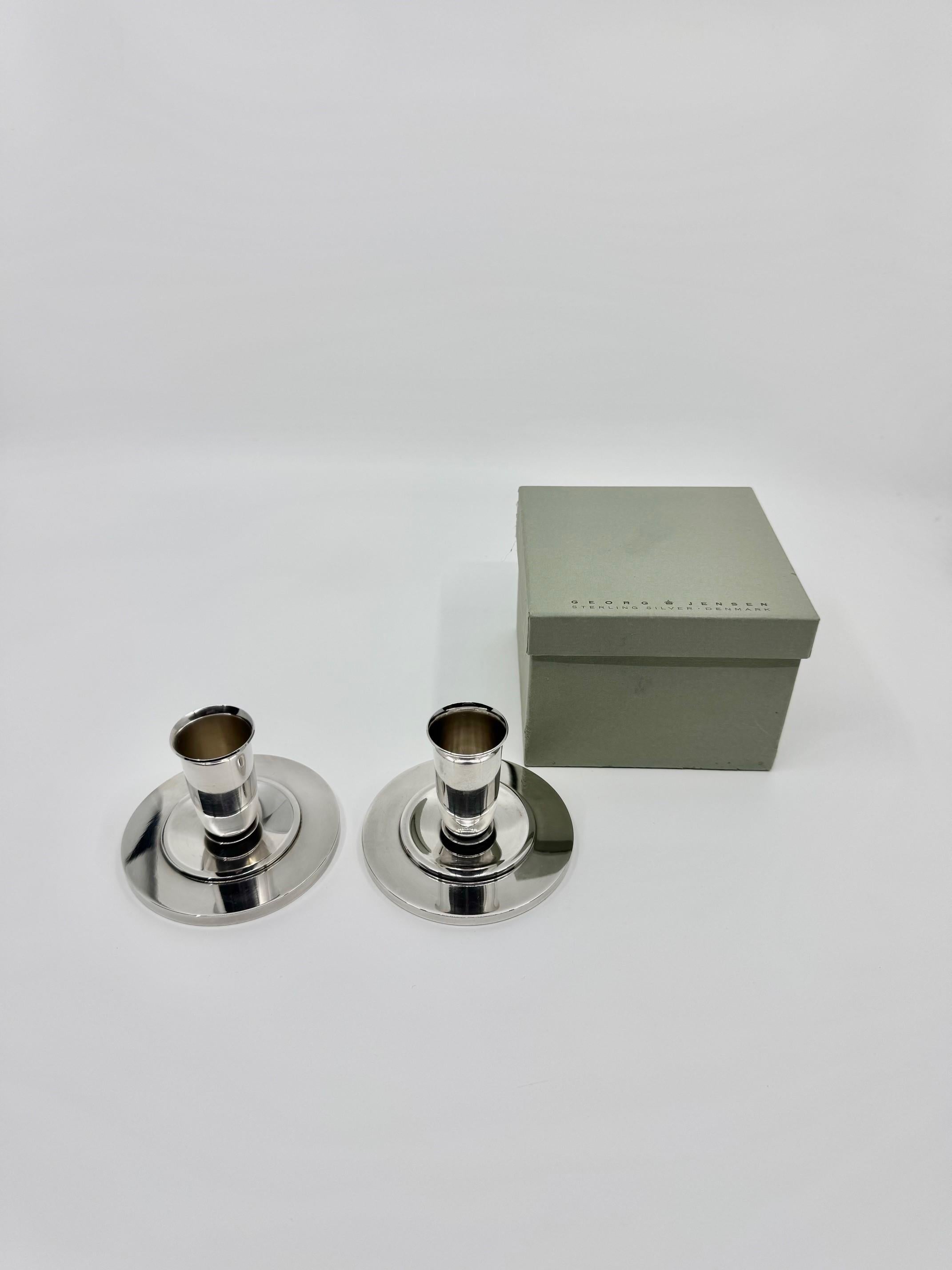 A pair of sterling silver Georg Jensen Art Deco candlesticks, design #748 by Harald Nielsen, dating back to the early 1930s. Each candlestick features a round base with a stepped transitional disc, accented by an oxidized ring, leading to a subtly