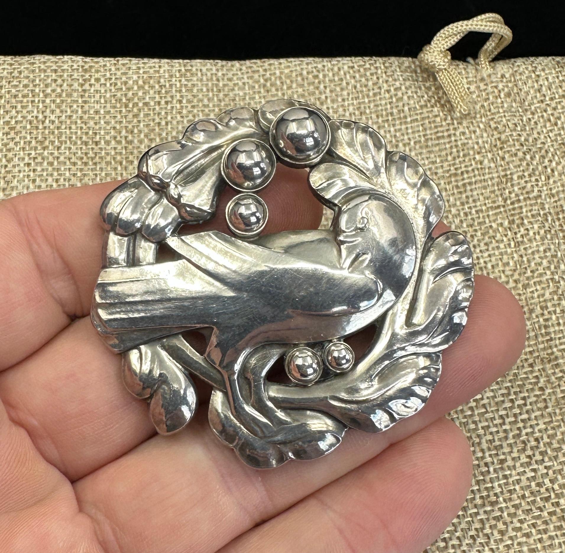 Diese große Brosche von Georg Jensen zeigt den klassischen Taubenvogel.
Diese seltene frühe Version weist fünf erhabene Silberperlen auf, die dem Jensen-Lorbeerkranz, der die Taube umgibt, hinzugefügt wurden.  Dies ist die größte Brosche von Georg