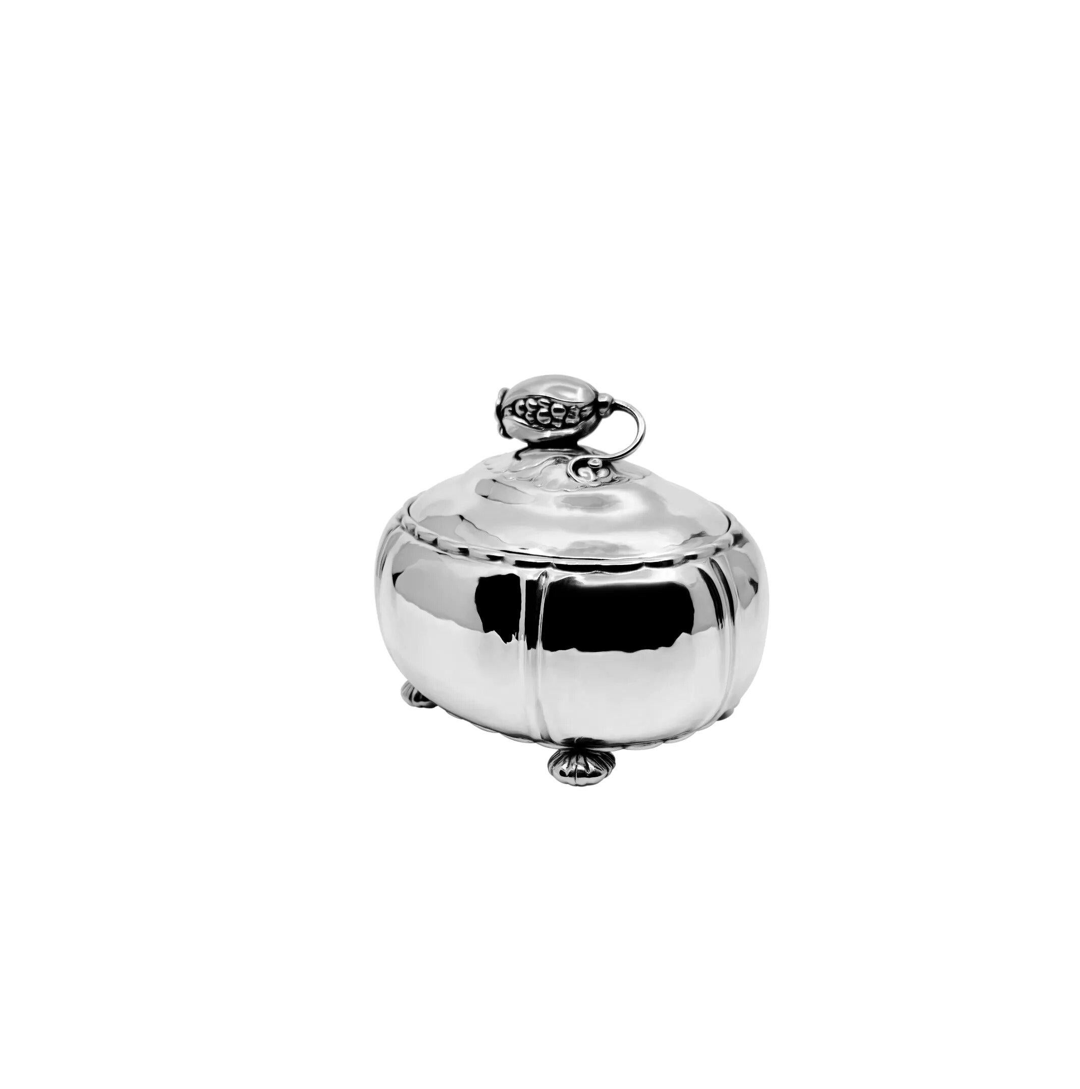 Antigua bombonera de plata de ley 830 de Georg Jensen, diseño nº 186 de 1918. Presenta un bombón con tapa ovalada hecho a mano con un intrincado grabado a mano. Los pies están adornados con un diseño floral cincelado a mano y son huecos, no de