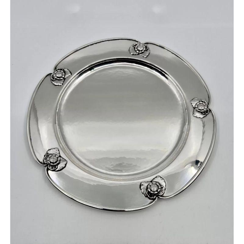 The rare Georg Jensen charger plate from circa 1927 is a sterling silver masterpiece. Design #491B showcases intricate floral motifs with visible hand-hammering. Its heavy, high-quality construction and curved edges surrounding the flowers exhibit