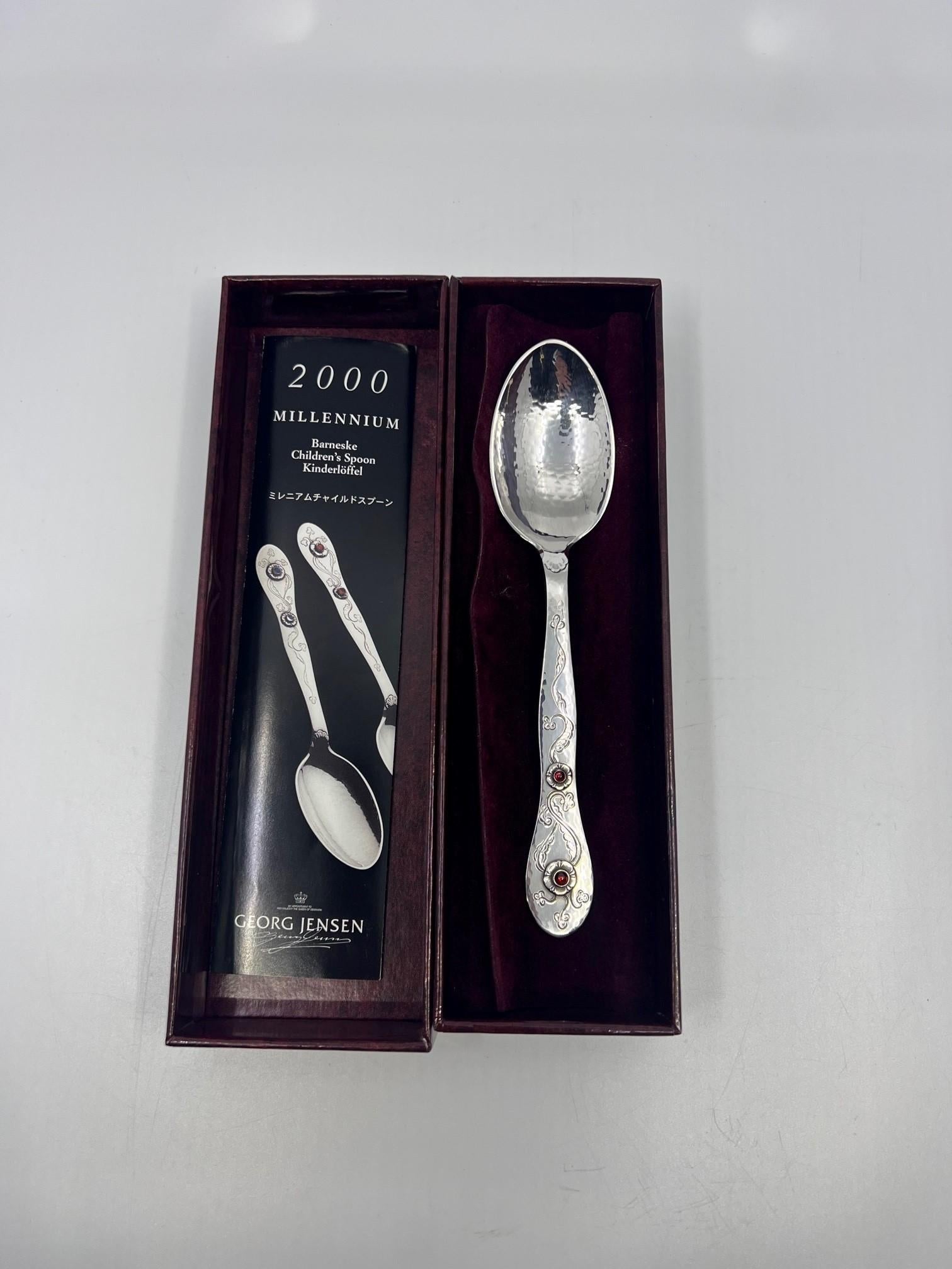 A Georg Jensen sterling silver 2000 Millennium spoon, with two set red garnet stones. New in the box along with the original brochure. This spoon was handcrafted in Denmark in 1999 and has a great deal of hand chasing.

Additional