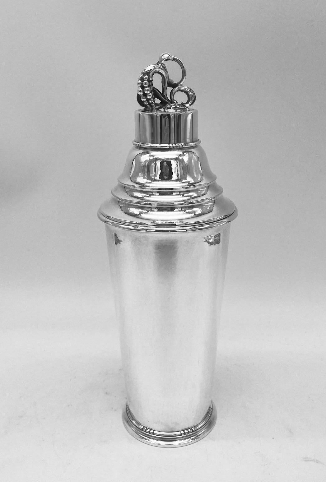 A large and stylish sterling silver cocktail shaker, made by the Danish firm of Georg Jensen and designed by one of their most important designers, Harald Nielsen.
The shaker is spot hammered all over, and has a bud and leaf finial on the removable