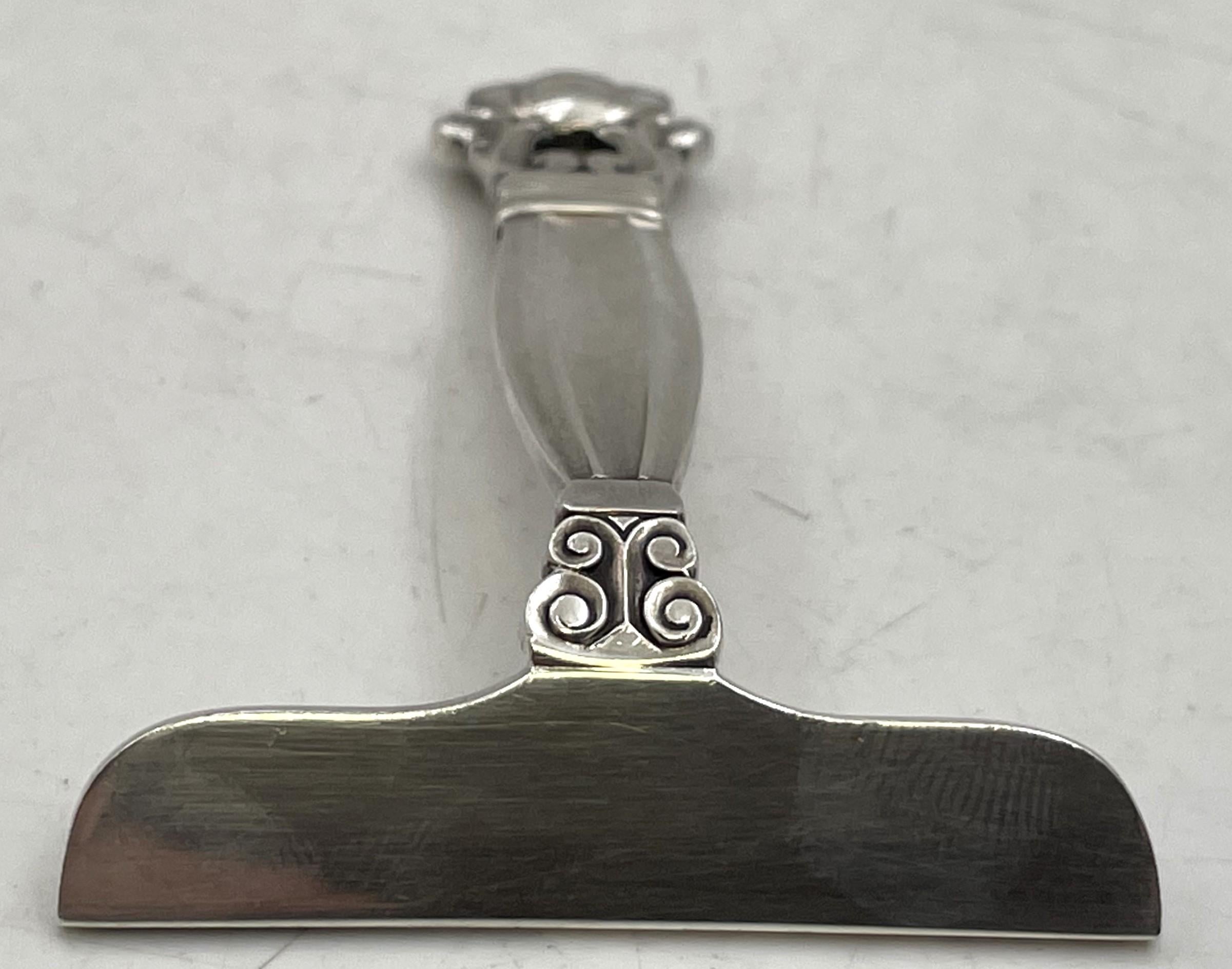 Empujador de alimentos Georg Jensen de plata de ley, con el célebre diseño de bellota, mide 3 3/8'' de largo por 2 3/4'' de fondo y 1/2'' de alto, y lleva los sellos que se muestran. 

El platero danés Georg Jensen (1866-1935) creó su propio negocio