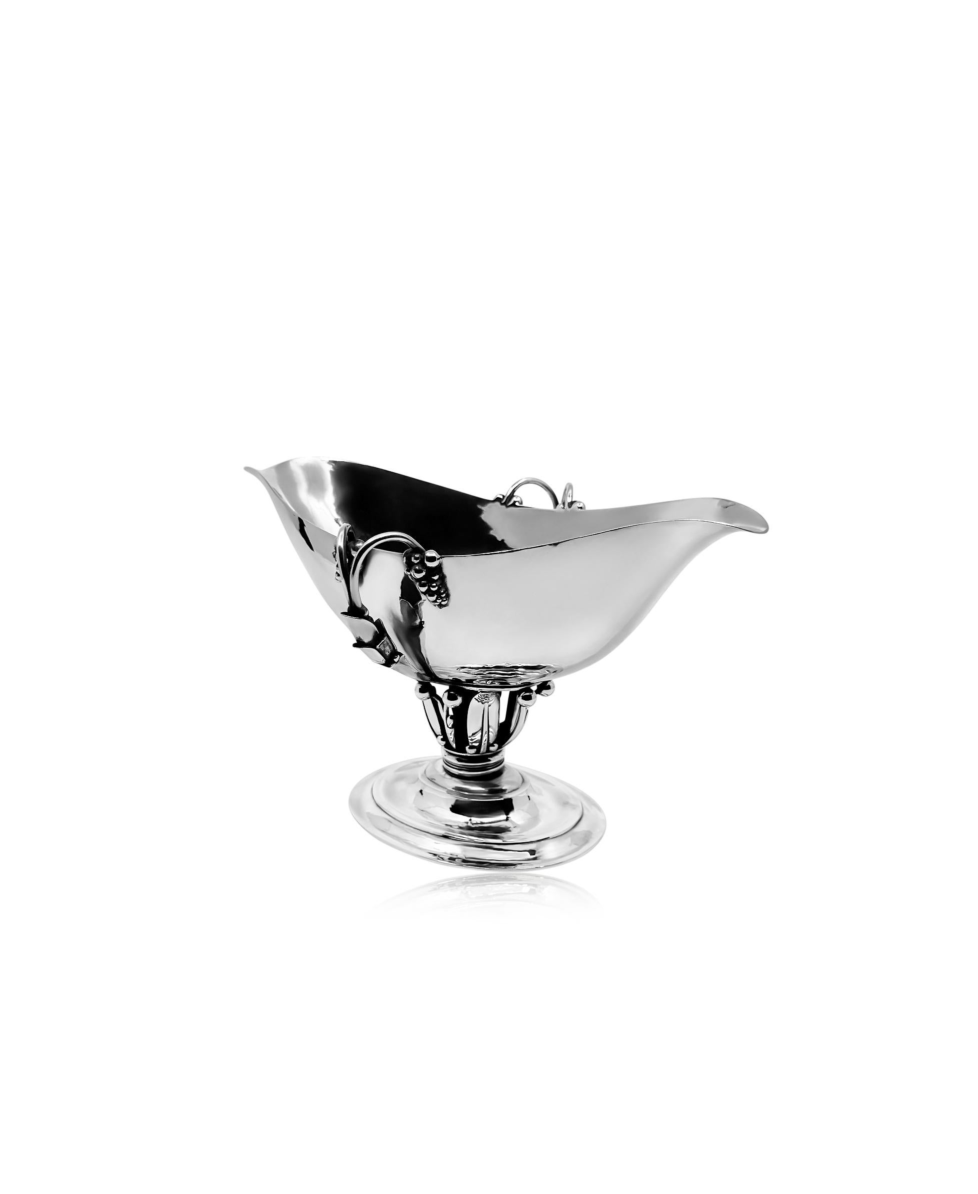 A generously proportioned vintage Georg Jensen grape sauce boat, featuring design #180 by Georg Jensen from the year 1918. This sizeable sauce boat boasts a distinctive double-spouted design, flanked on each side by two substantial grape clusters.