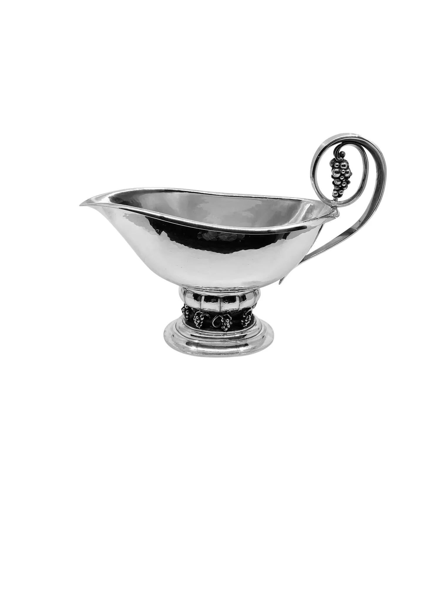 Una salsiera Georg Jensen extra-large con l'iconico disegno dell'uva, il motivo #296, creato originariamente da Georg Jensen nel 1924. Questo pezzo presenta una base ovale sostenuta da un piedistallo ornato da otto grappoli d'uva lavorati in modo