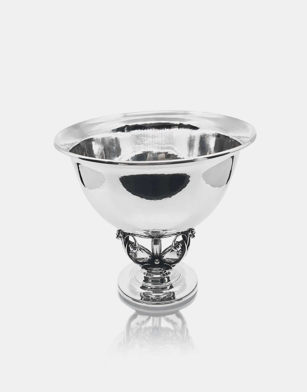 A large Georg Jensen sterling silver ornate grape bowl, design #468A by Gundorph Albertus from 1926. The bowl serves as a weighty centerpiece, elegantly poised on three delicate, leaf-shaped supports adorned with floral motifs. Each of these floral