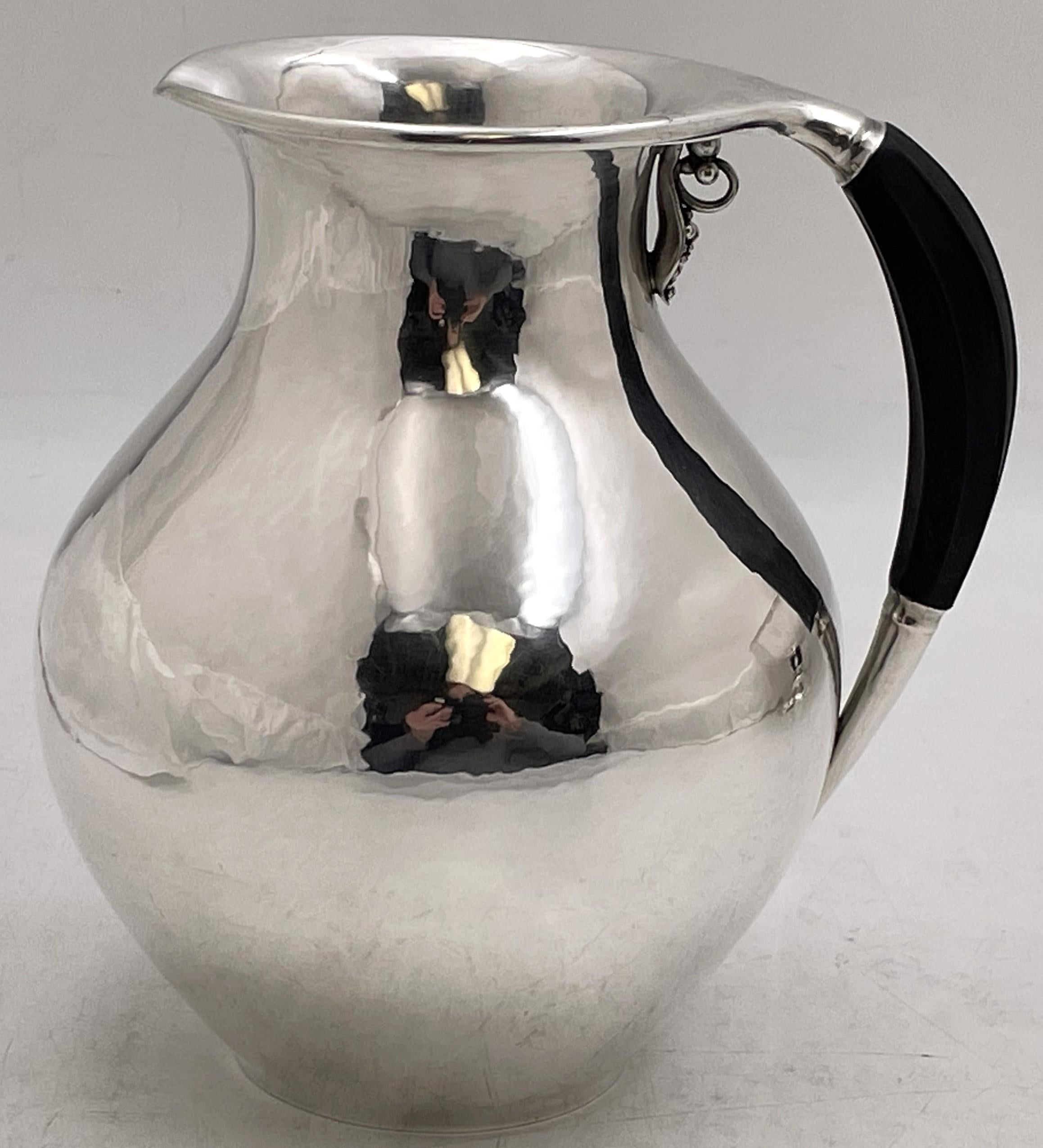 Georg Jensen sterling silver pitcher in pattern number 385A, made in the 1930s, beautifully hand hammered and showcasing stylized natural motifs. It measures 6 7/8'' in height by 5 3/4'' from handle to spout, weighs 17.8 troy ounces, and bears