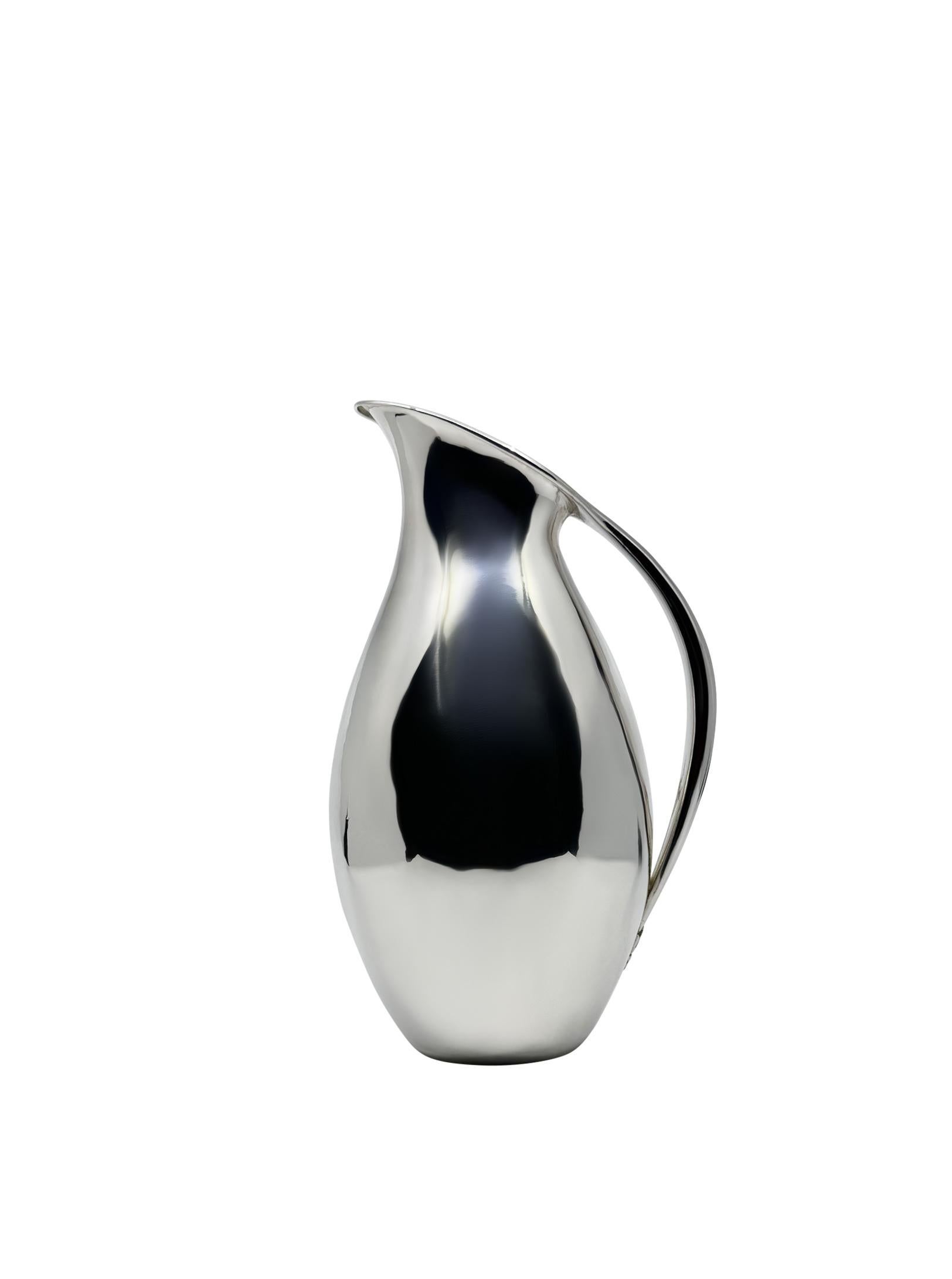 Una jarra de plata de ley Georg Jensen, diseño nº 432A, ideada por el renombrado artista Johan Rohde en 1920.  Conocida por su elegancia atemporal y su innovador aspecto minimalista, esta jarra icónica sigue siendo un testimonio del visionario Johan