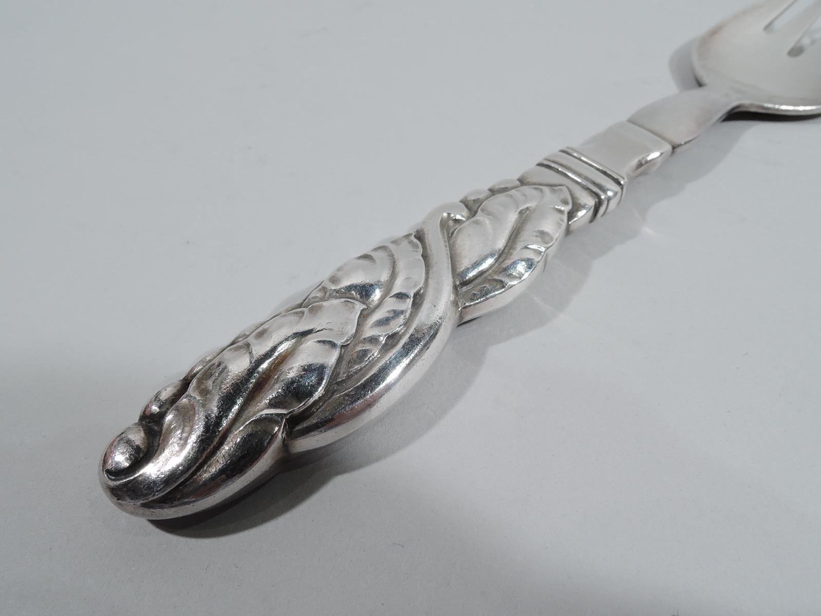 Ornamental sterling silver serving fork. Made by Georg Jensen in Copenhagen. Handle leaf-wrapped and entwined with scrolls. Bottom edged with kernels or seeds. Hand-hammered shank with 4 tines. Illustrated in: Drucker. Georg Jensen, 2001, 2nd rev.