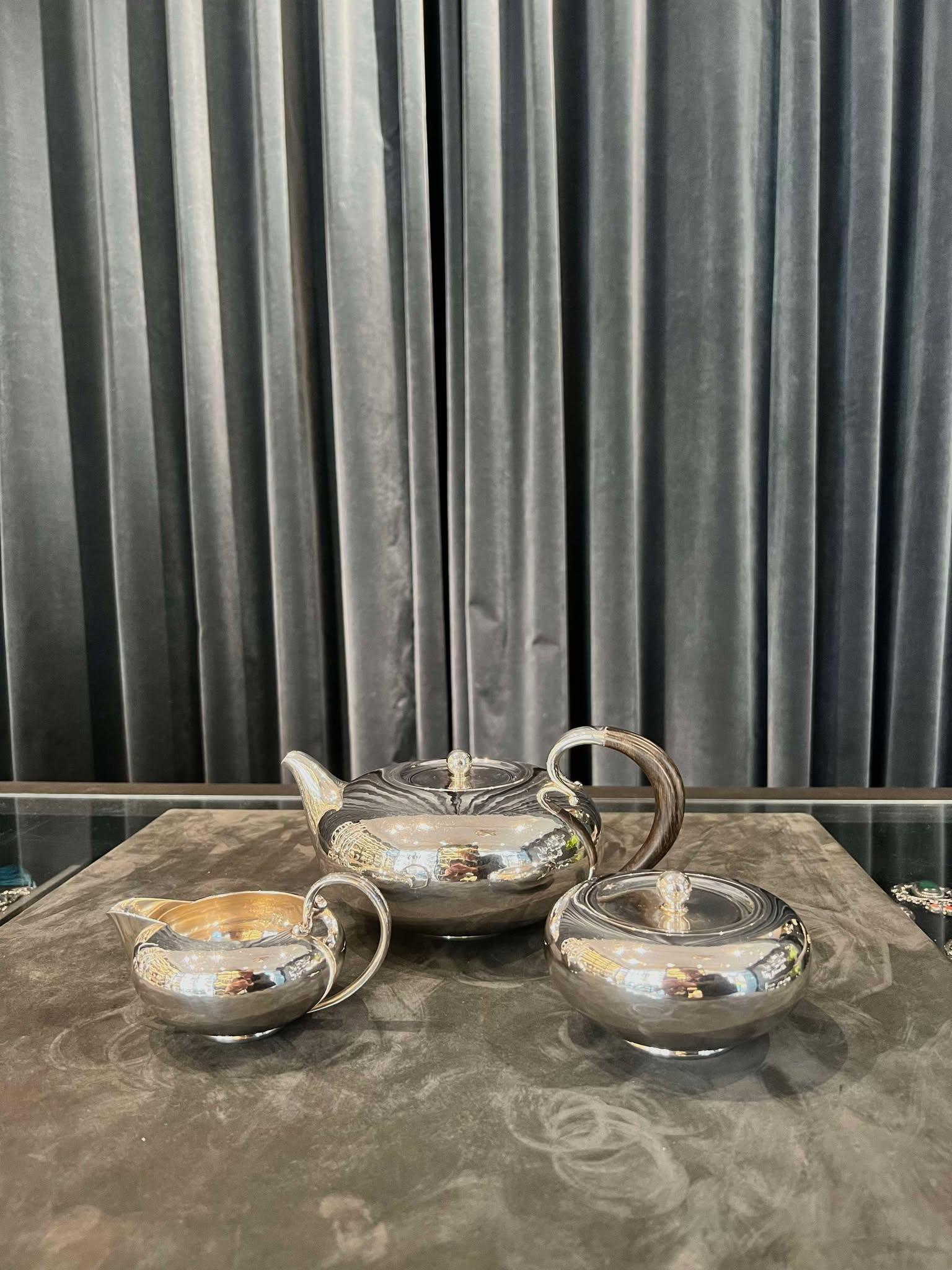 Un servizio da tè Georg Jensen in argento sterling d'epoca con manici in ebano, design #787 di Johan Rohde del 1933. Questo è uno degli ultimi disegni di Johan Rohde prima della sua scomparsa nel 1935. La teiera martellata a mano è caratterizzata da