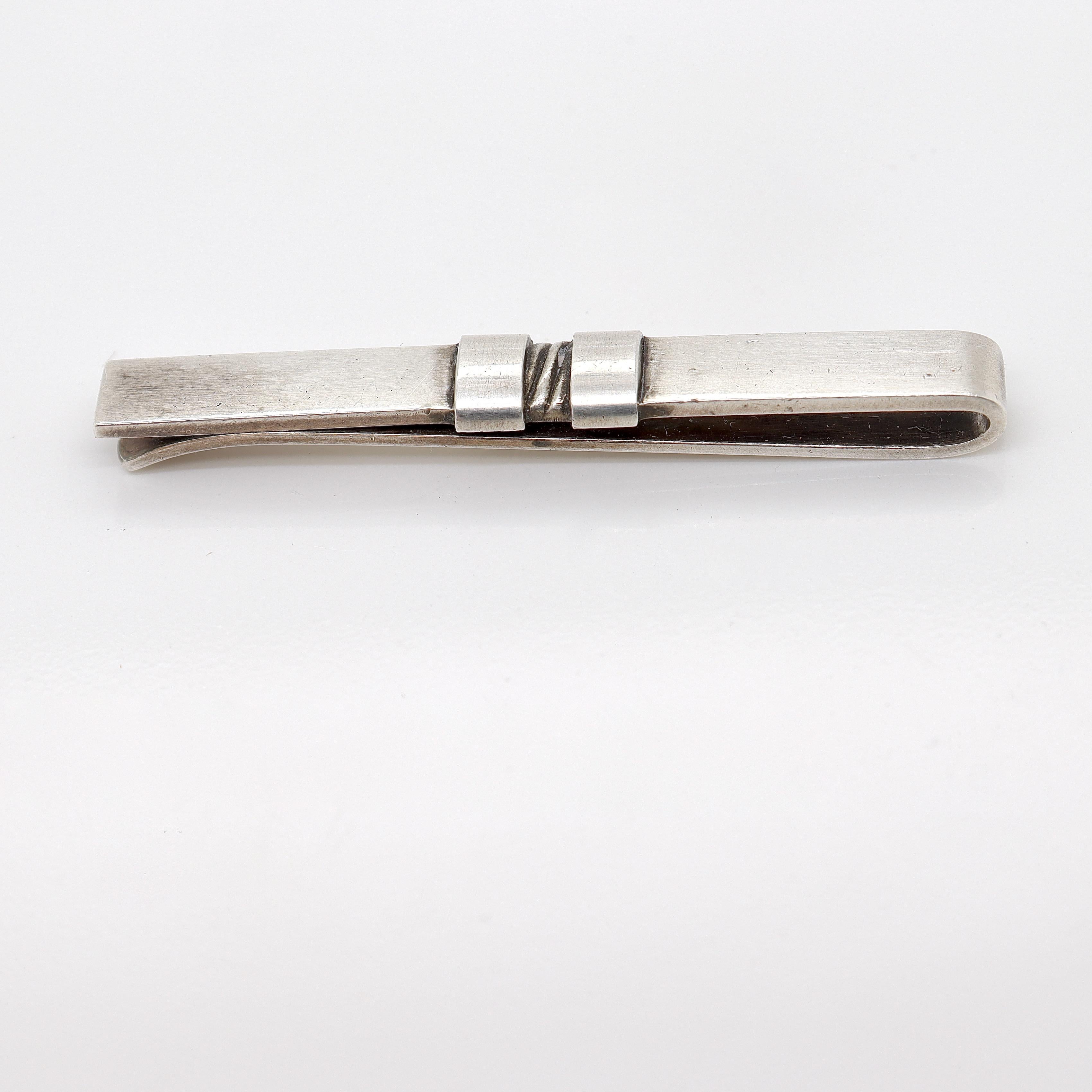A fine Georg Jensen sterling silver tie clip. 

Model no. 74.

Designed by Sigvard Bernadotte for Georg Jensen circa 1953.

And of course, it can double as a money clip.

Simply a wonderful piece from one of Denmark's premier