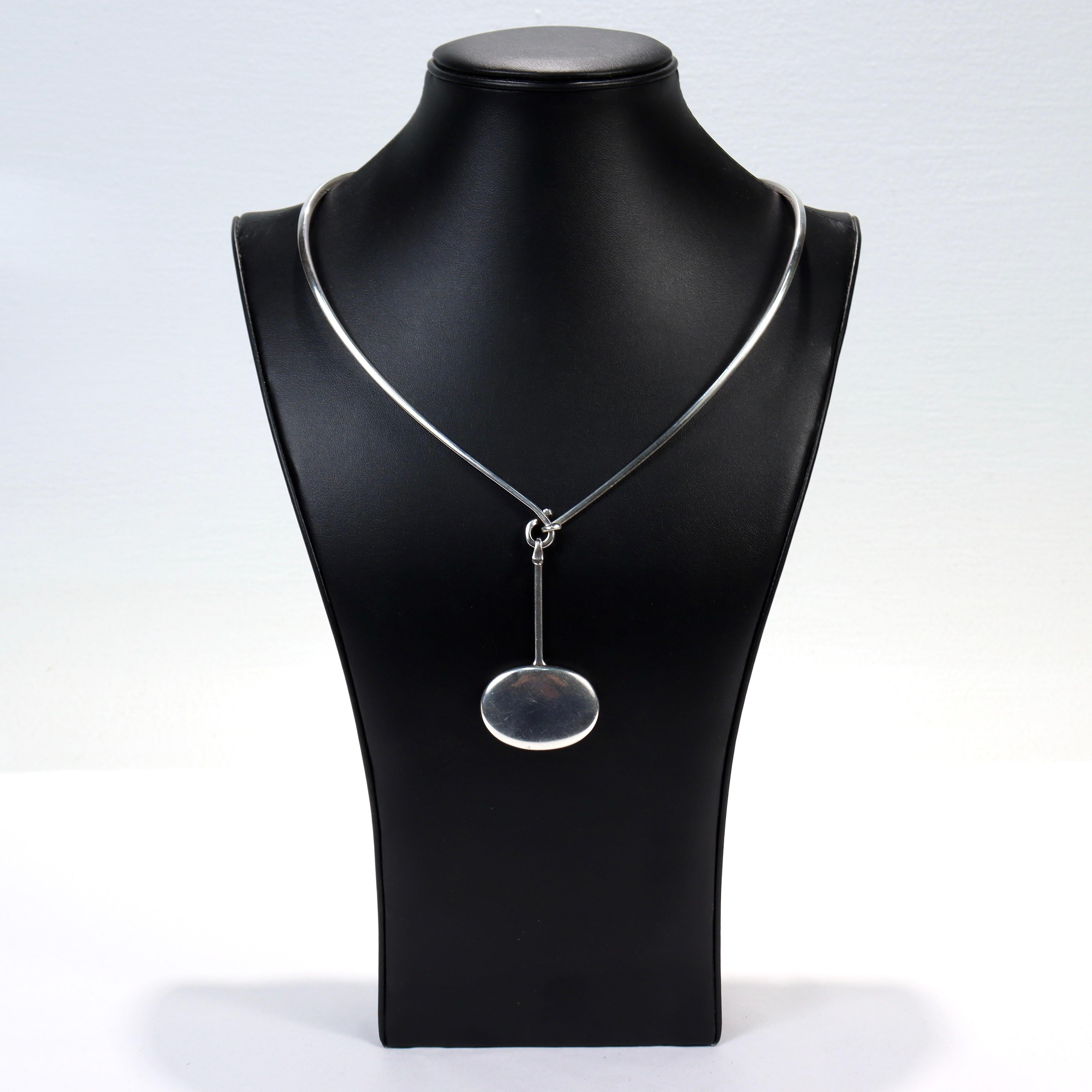 A fine Georg Jensen sterling silver necklace.

Designed by Vivianna Torun Bulow-Hube, who designed under the pseudonym Torun. 

Comprised of the shaped neck piece no. 167 and a silver pendant no. 304.

Together with its original Georg Jensen felt