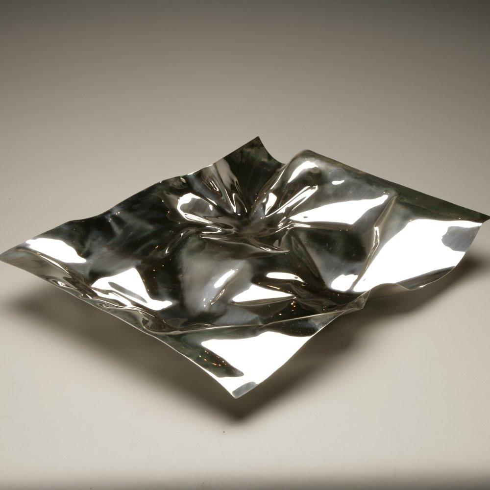 Georg Jensen sterling silver tray no 1302. 

Designed by Verner Panton in 1988. It is a beautiful mirror-polished dramatic centerpiece. 

Designer: Verner Panton
Maker: Georg Jensen
Design #: 1302
Circa: new production
Dimensions: 21.7
