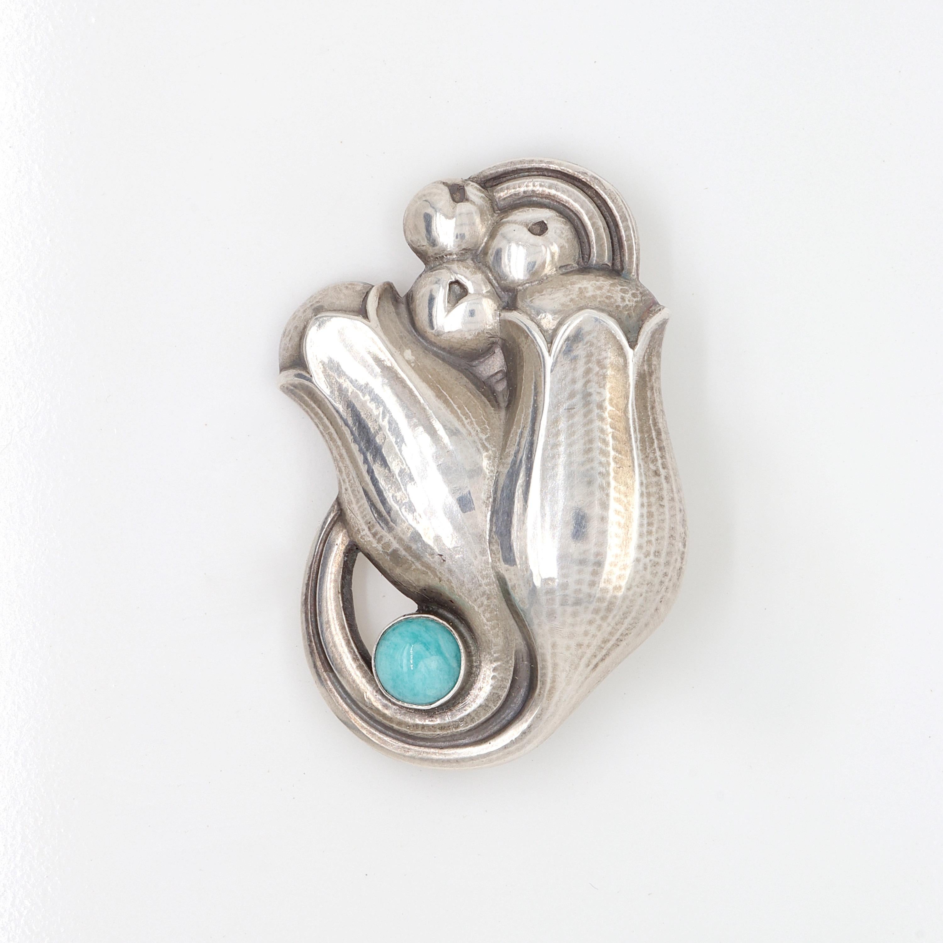 A fine Georg Jensen sterling silver pin or brooch.

Model no. 100B.

Designed by Georg Jensen.

In the form of hand-hammered, stylized tulip flowers and berries and with an amazonite cabochon.

Simply a wonderful brooch from Denmark's premier