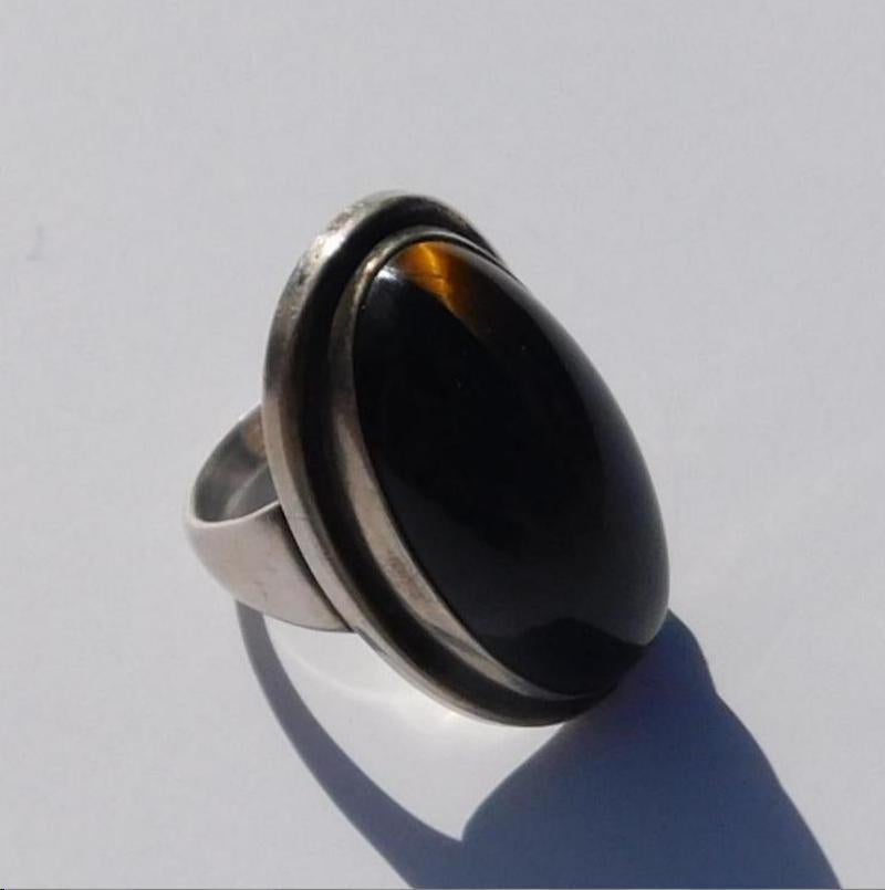 Danish Modernist Georg Jensen Classic Mid-Century Modern sterling silver ring with a large 
tiger's eye cabochon stone created circa 1940s-60s.
Excellent silver work with a subtle curve set with a striking oval shaped dark tiger’s eye stone with