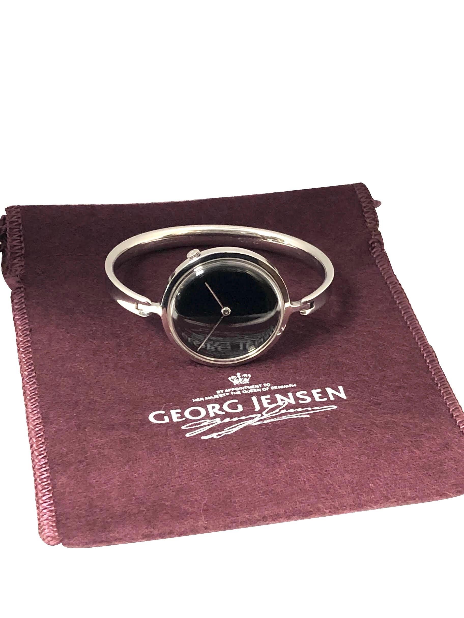 Circa 1990s Georg Jensen Vivianna Bangle Watch By Torun. Measuring 1 1/4 inch Diameter with the watch attached to a 3/16 inch wide bangle bracelet with a 6 1/2 inch inside measurement. Quartz Movement, Black mirrored Dial. Comes in a Georg Jensen