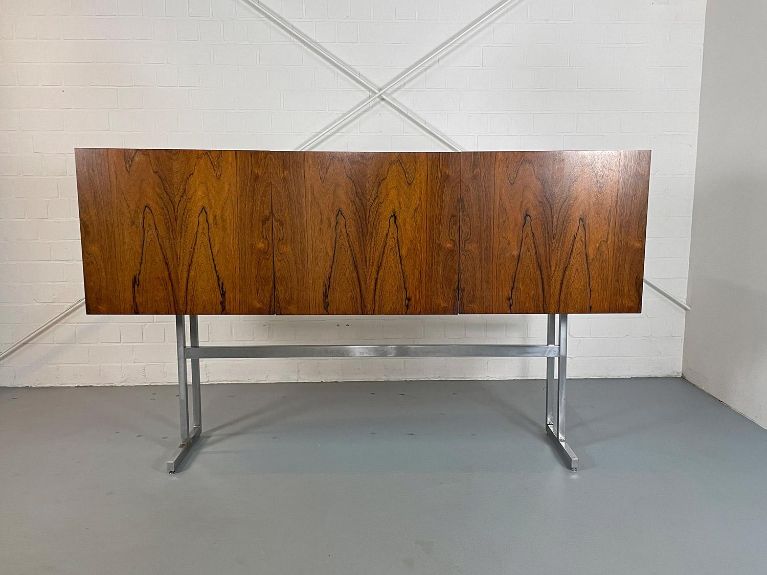Rare highboard designed by Georg Satink for WK Wohnen in the 1960s. An absolute eye-catcher together with the high chrome frame. The three doors can be folded out to the front.