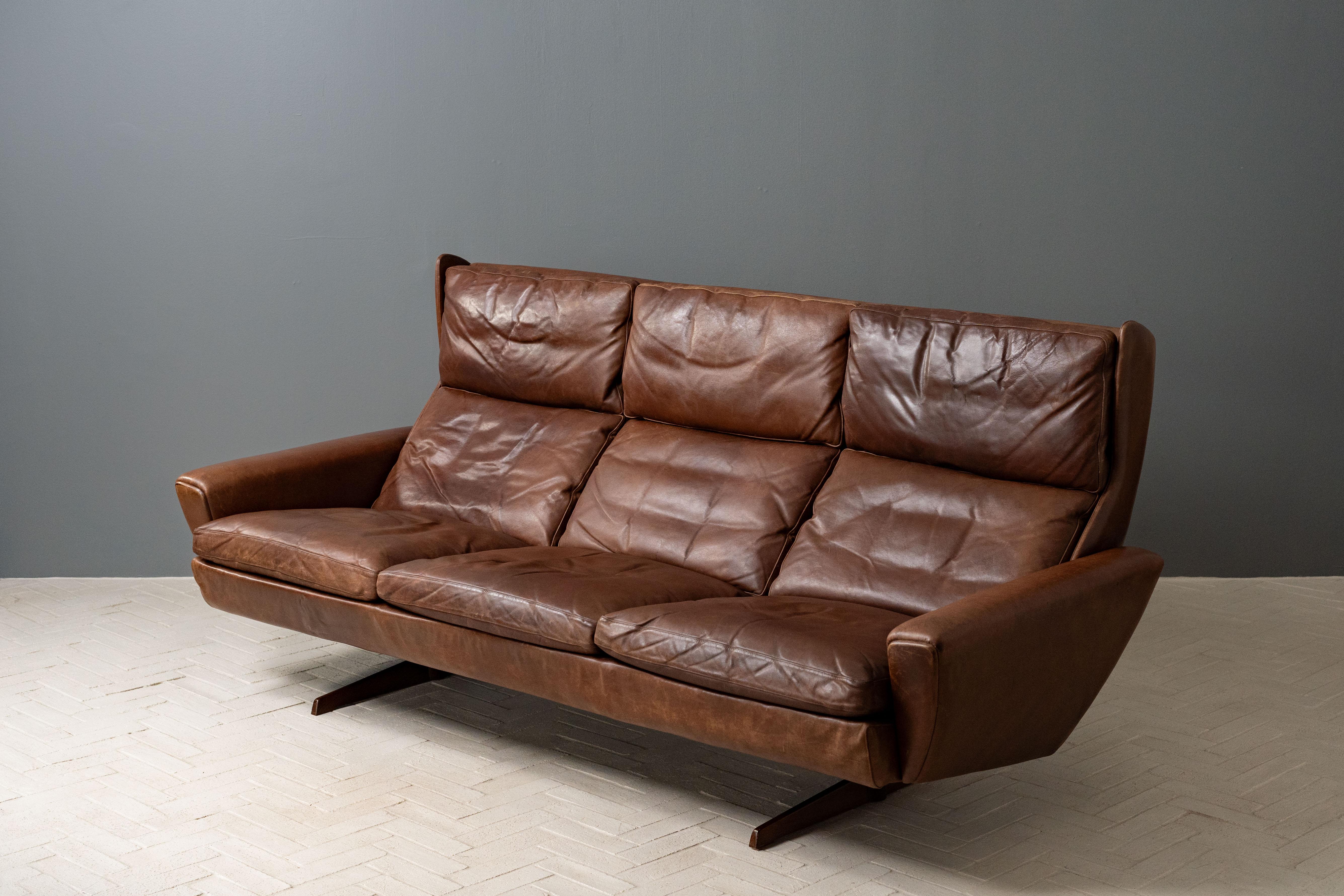 Denmark, ca. 1960s. A scarce and stylish three-seat sofa by Georg Thams for Vejen Polstermøbelfabrik. Features incredibly heavy construction with original deeply patinated brown leather upholstery. Slouchy down-filled cushions have that perfect old