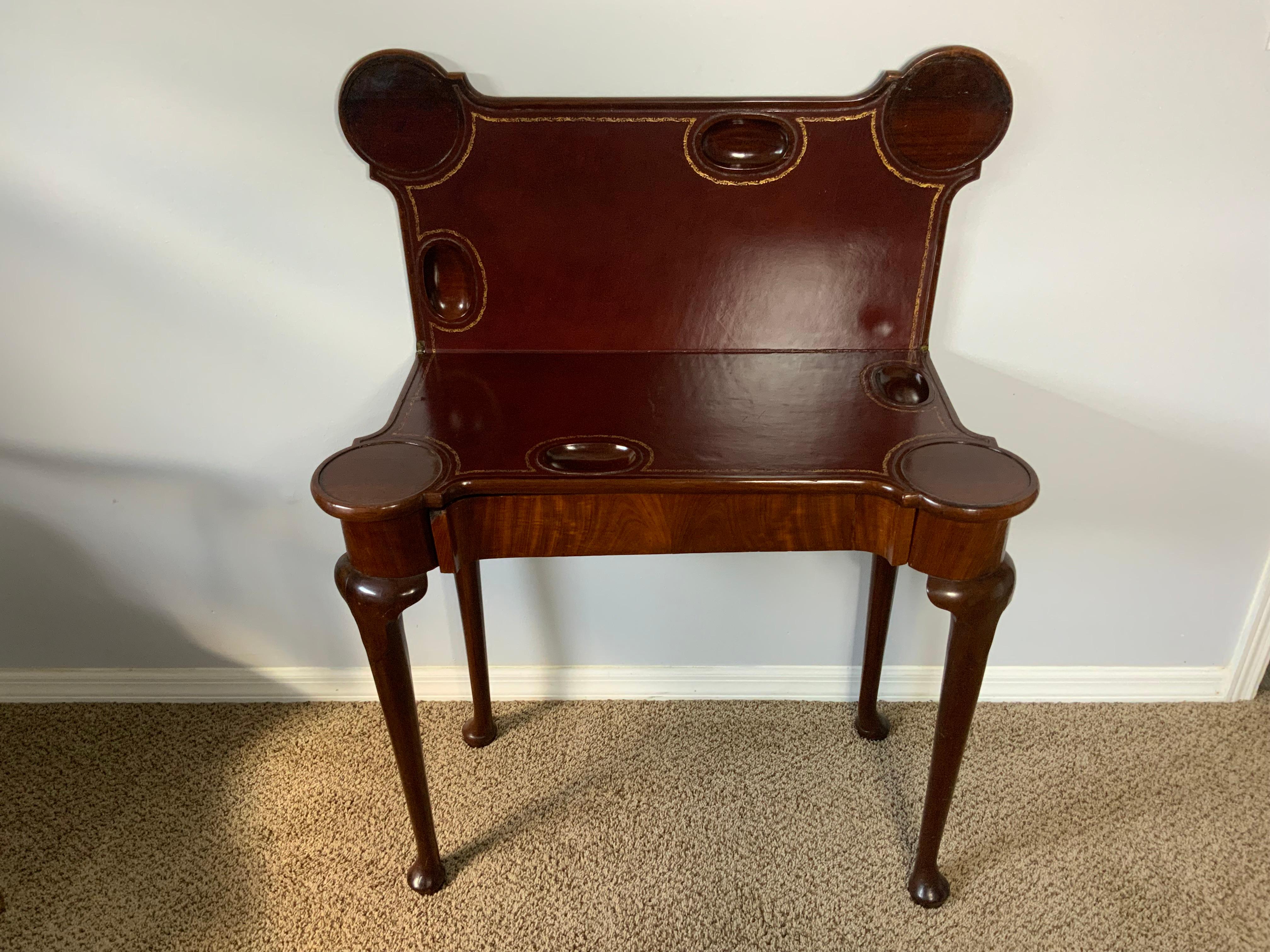 Tavolo da gioco pieghevole in mogano del periodo Giorgio II con cassetto nascosto sul fregio anteriore, piano rettangolare con angoli arrotondati e sagomati sporgenti, sollevato su quattro gambe con caratteristici dettagli intagliati a lappet sulla
