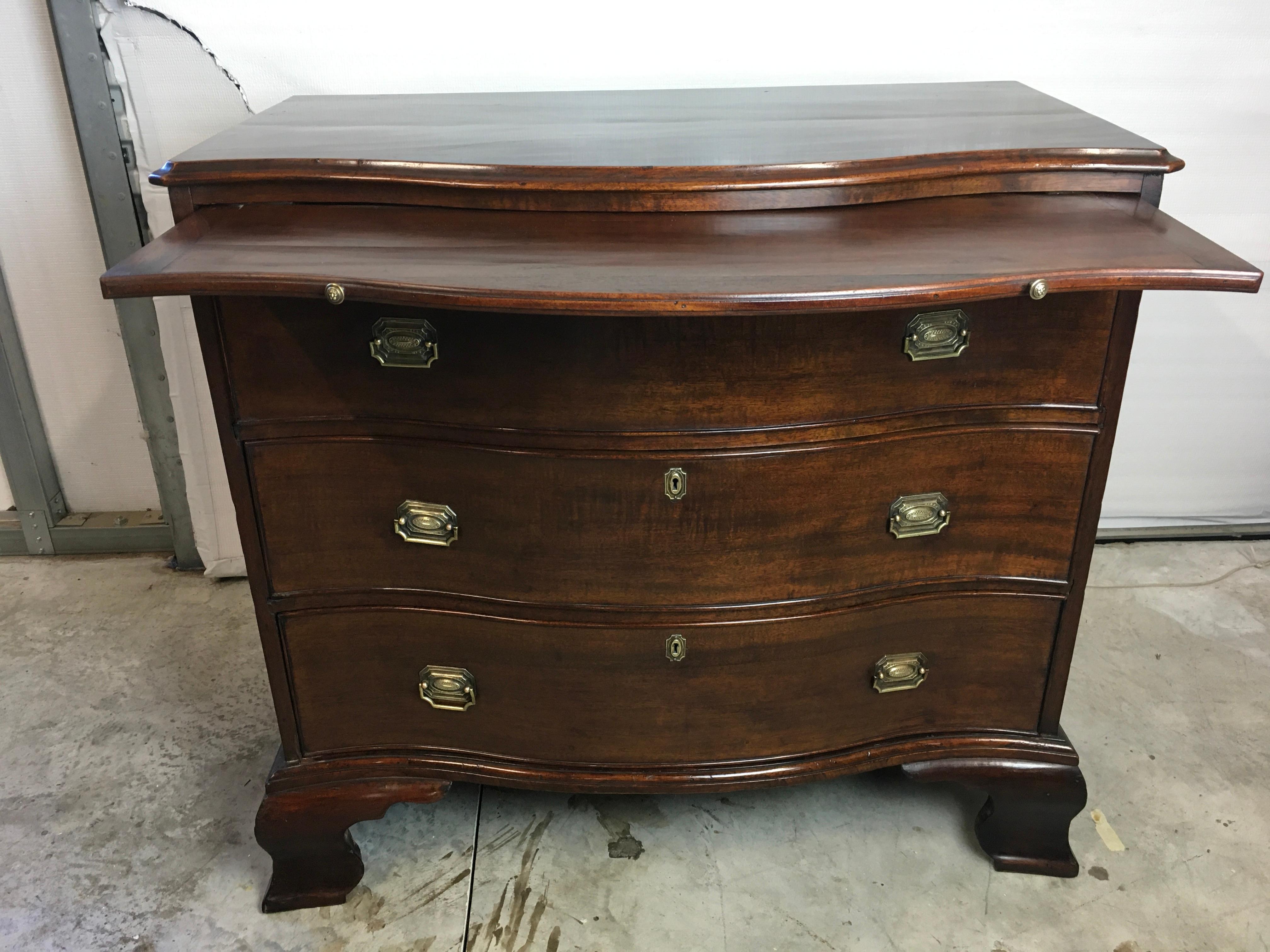  Georgian Mahogany serpentine front bachelors chest resting on tall ogee bracket feet 1790-1800.  Nicely figured solid Cuban Mahogany molded edge top over a pull out brushing slide and three large graduated cock beaded drawers. Secondary woods are