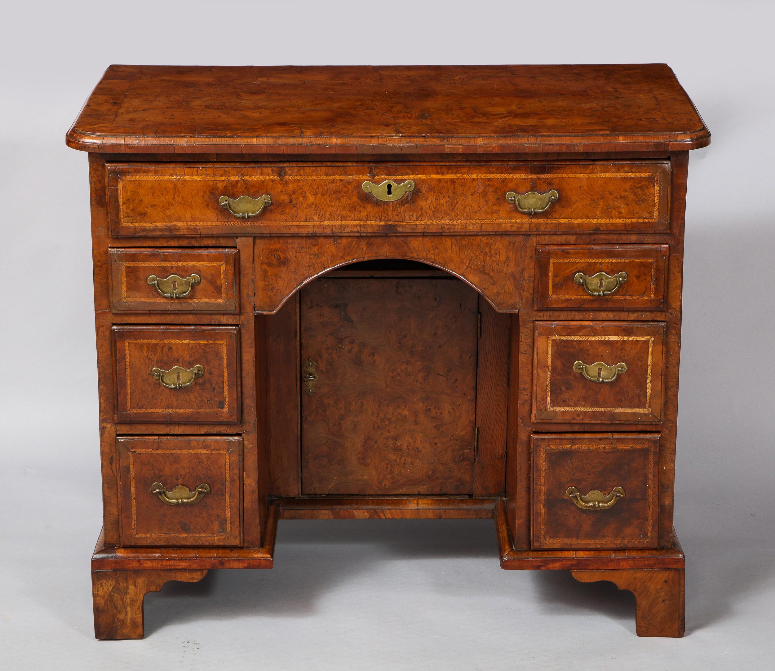 Rare early 18th century yew wood kneehole desk or dressing chest, the patchwork veneered and shaped top with rounded corners and molded edge over long single drawer and two banks of small drawers, the center with sunken door, the whole standing on