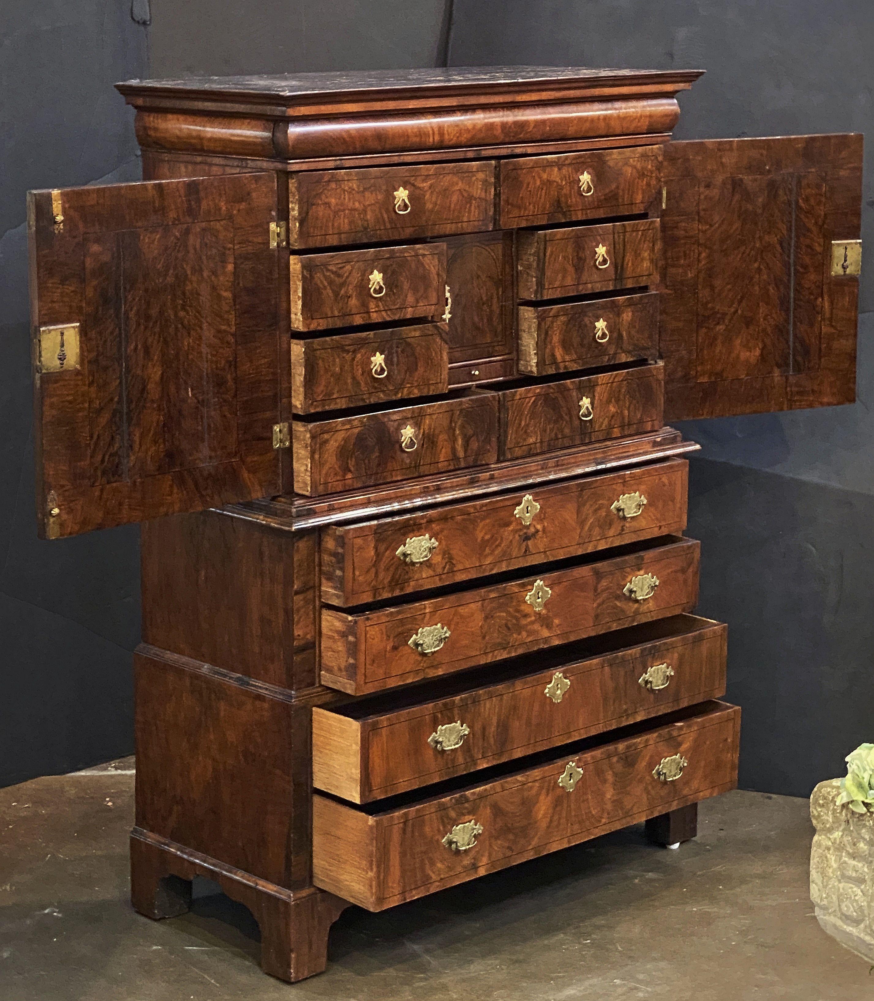 A fine large English period George I cabinet on chest of patinated walnut from the 18th century.
Featuring burr walnut-figured veneers and attractive brass hardware throughout. 

The top tier with cavetto cornice over a cushion moulded chart drawer