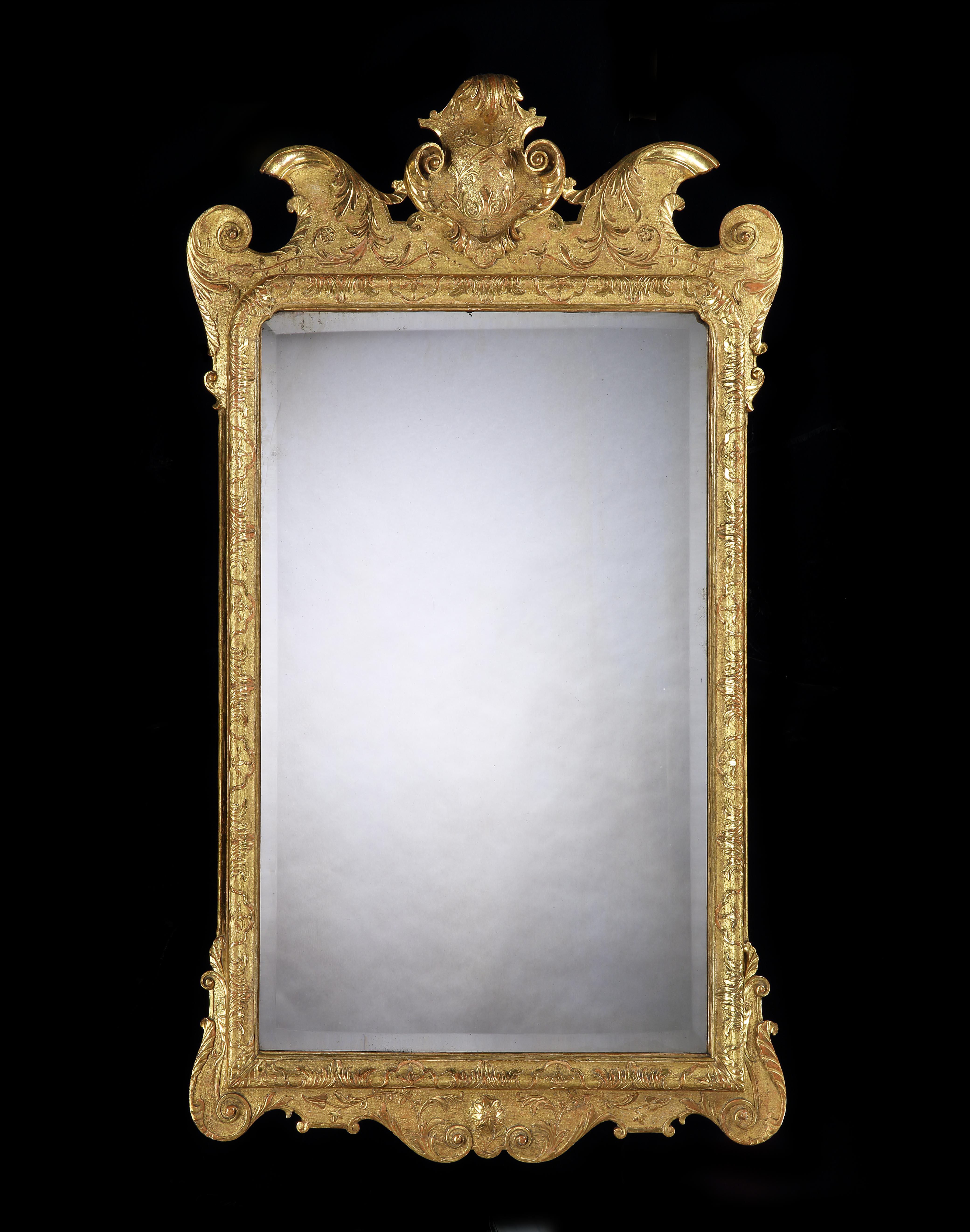 A George I carved and gilded gesso mirror with a stippled background and detailed carved foliage, the shaped cornice with a central cartouche, with bold scrolls to the sides. The 18th century bevelled plate surrounded by a frame similarly carved.