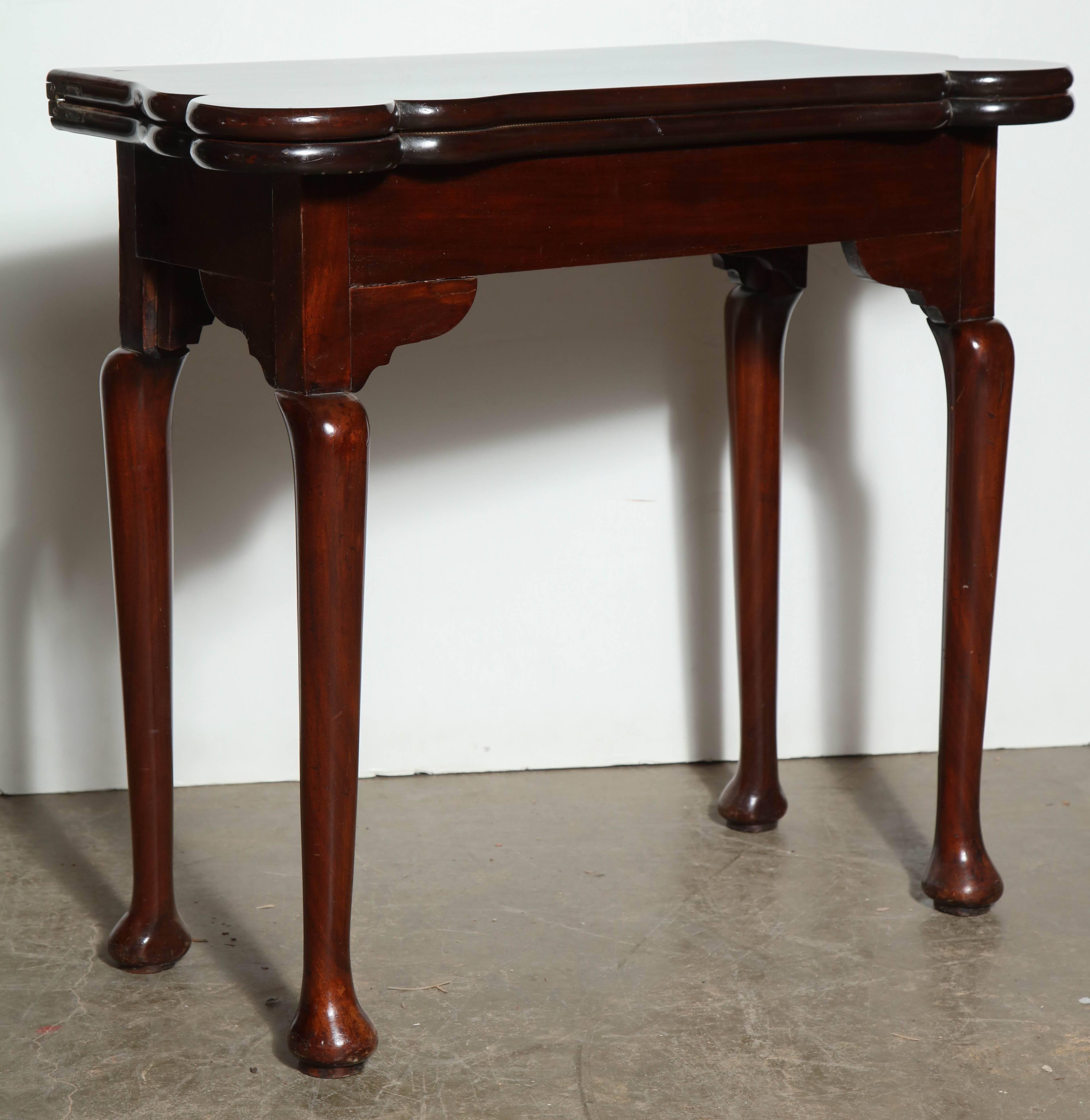 A rare English George I mahogany turret corner fold over game table with concertina action legs, fitted interior with candle and money recesses, floral upholstered top on turned legs and pad feet.