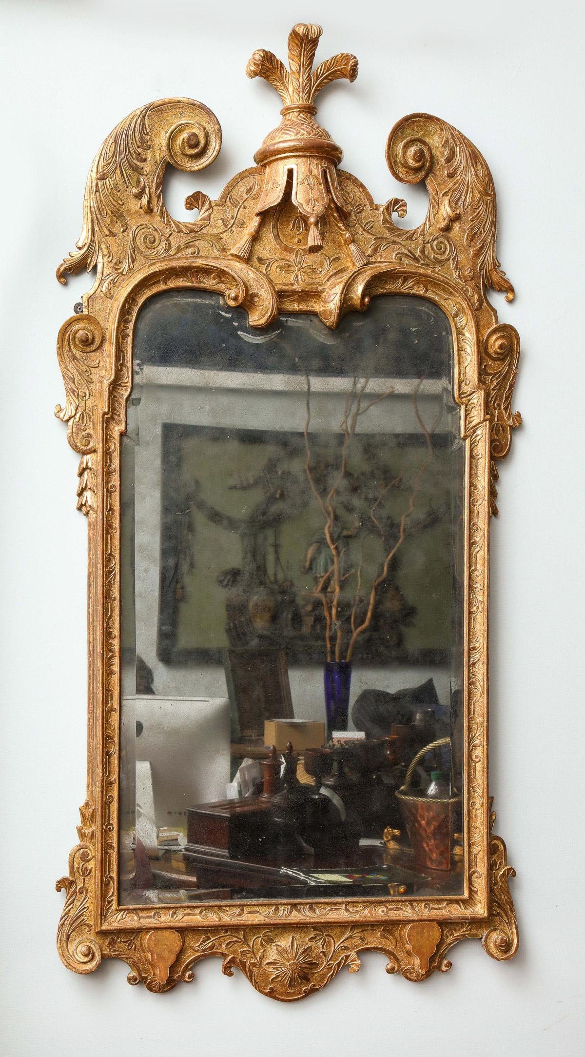 Very fine George I carved and gilt mirror, circa 1720, in the manner of John Belchier having an ostrich feather plume over tasseled central lambrequin, deep projecting scroll carved flourishes, the original beveled mercury glass plate having