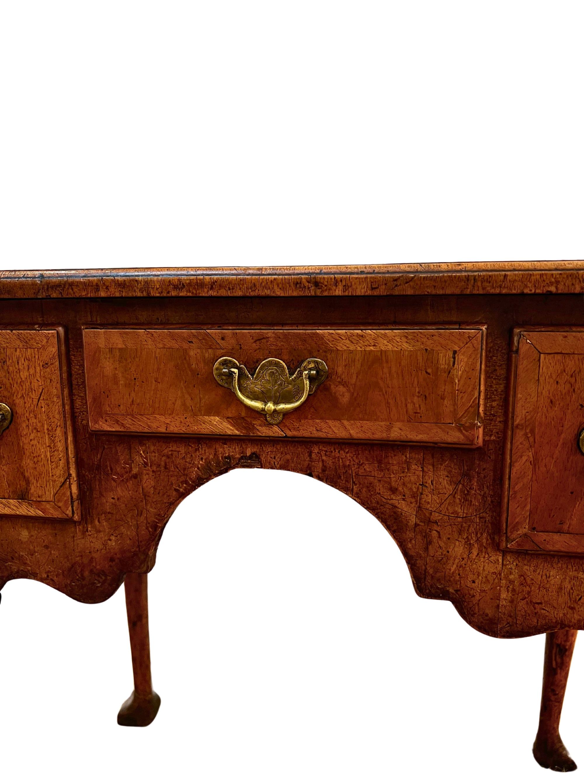 This early 18th-century walnut lowboy features cabriole legs, pad feet, and feather-banded drawers with an elegant arched apron. A fine example of early Georgian craftsmanship, it combines functionality with timeless design. Perfect as a statement