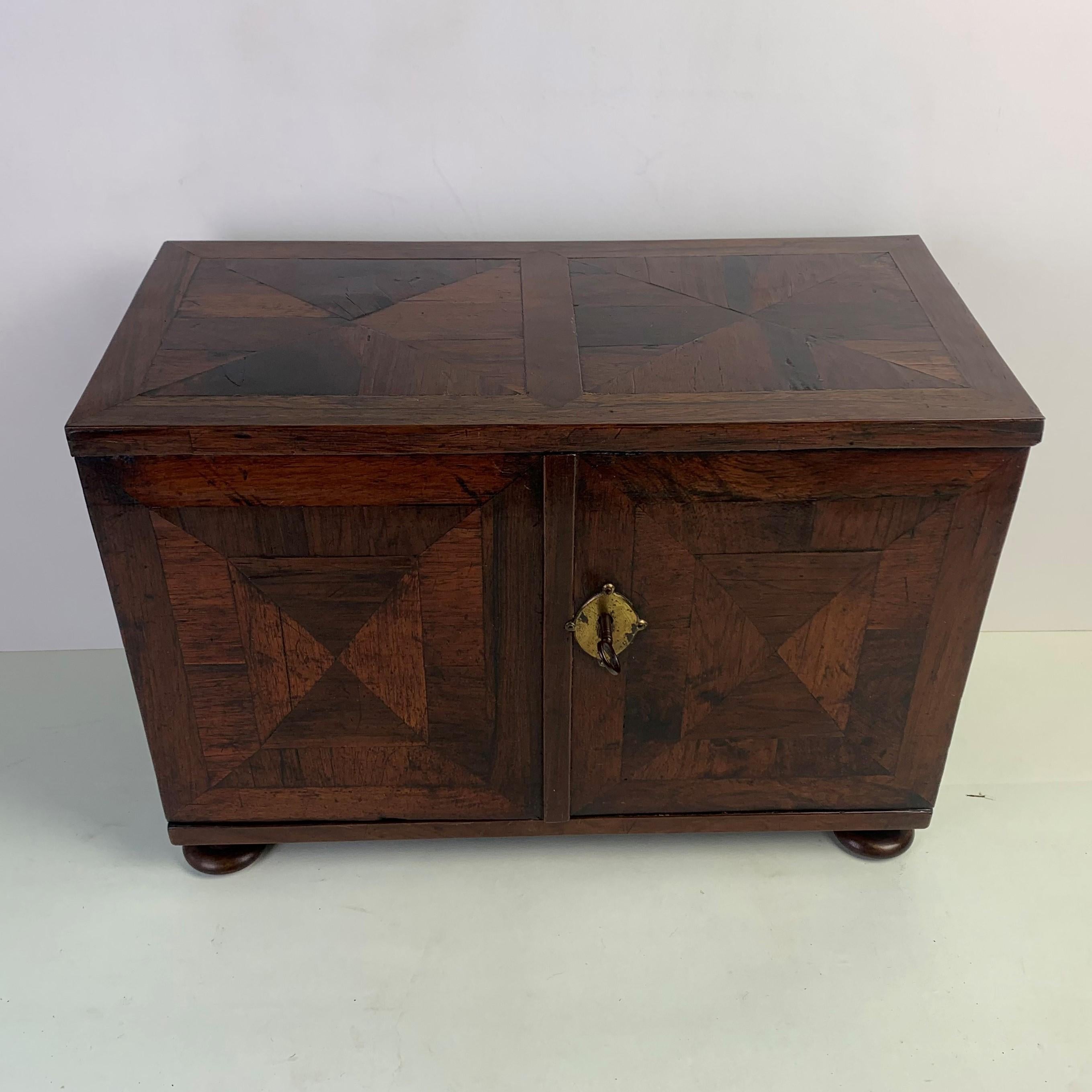A rare, early 18th cenury parquetry table top spice cabinet unusually veneered in rosewood set in a geometric pattern. The two doors opening to reveal an arrangement of seven drawers and matching rosewood veneers to the insides of the