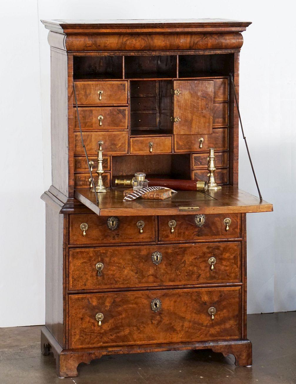 A fine English period George I secretary bureau escritoire or scriptor of figured patinated walnut from the 18th century featuring original split pin brass drop handles throughout. 
The top tier with ogee canopy long drawer over cabinet fall.
The