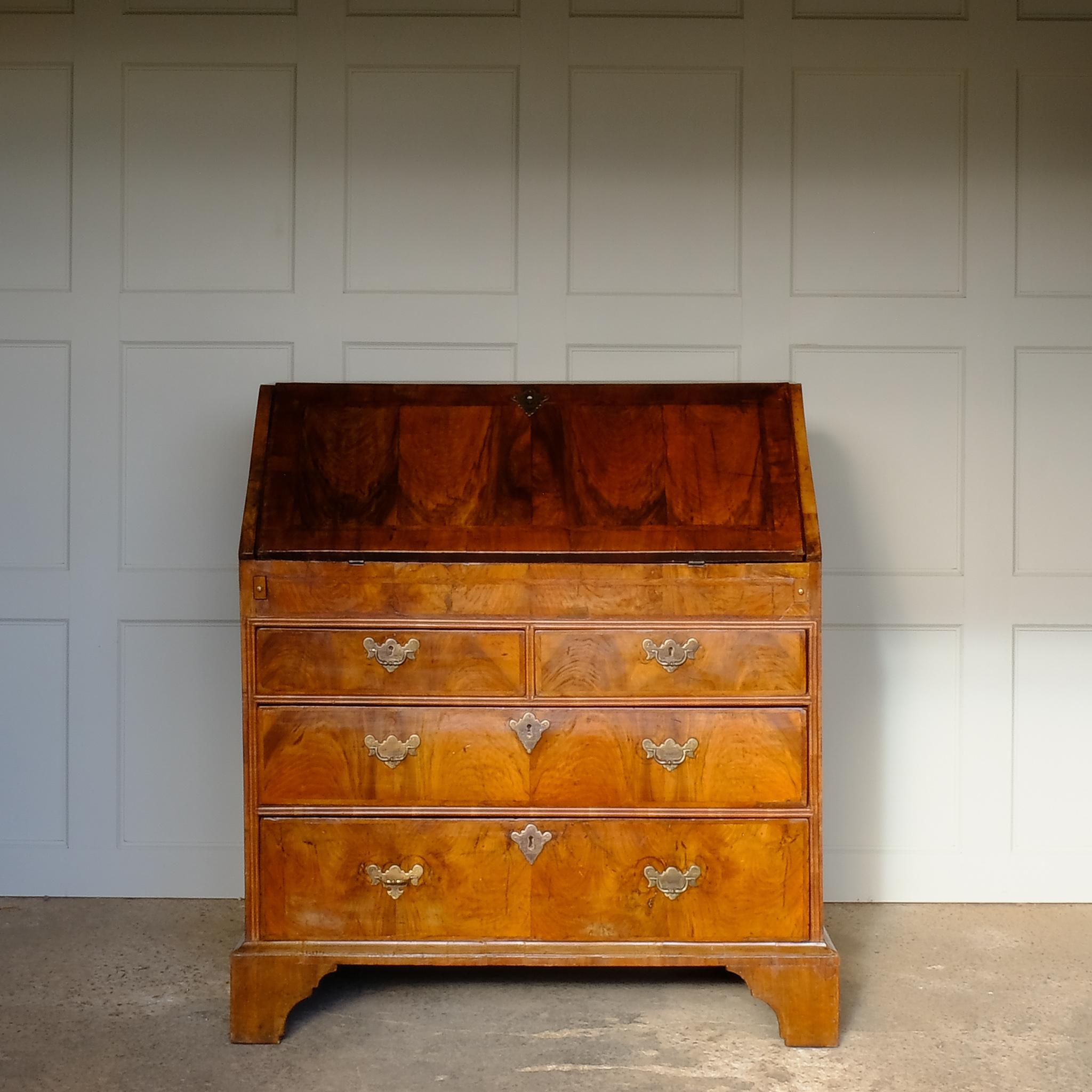 A George I Walnut Bureau, a beautiful and very original example. The fall-front over two short and two long drawers. Internally a central cupboard is surrounded by six drawer fronts and pigeonholes and a secret hideaway drawer, with a new green felt