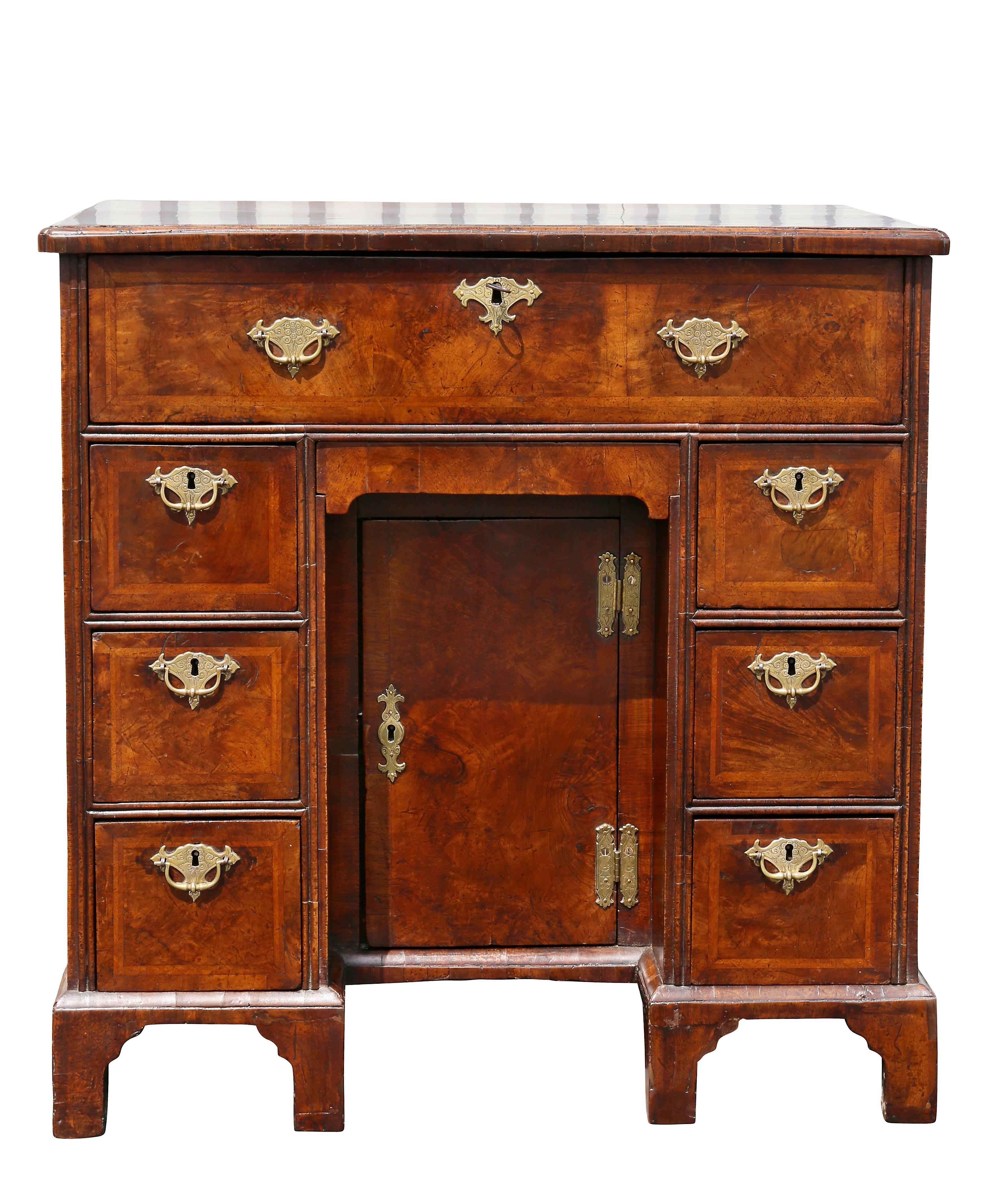 Nicely figured walnut, rectangular quarter veneer top over top over a drawer and kneehole with door and small drawer flanked by drawers raised on bracket feet.