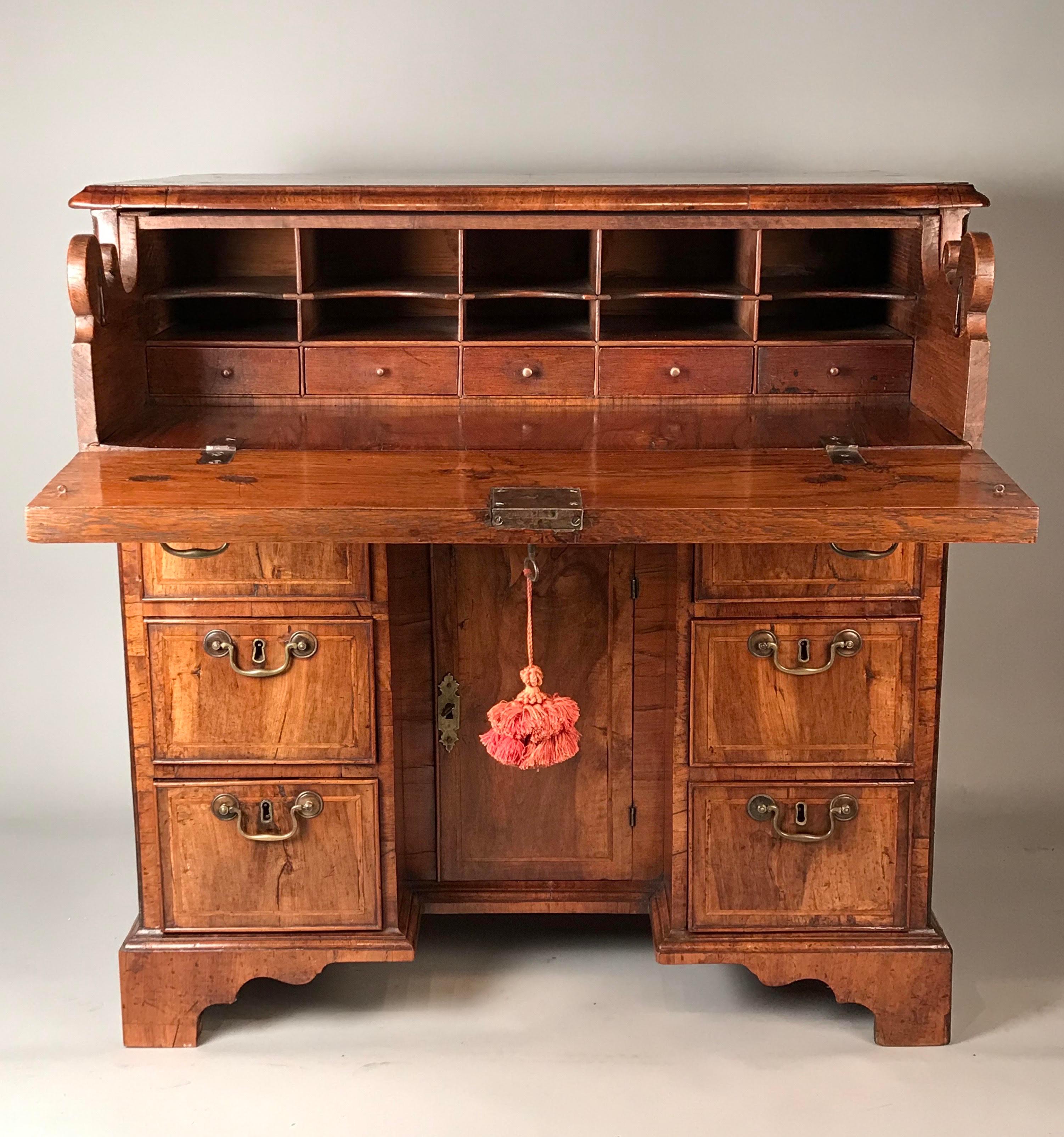 An English early 18th century walnut secrétaire kneehole desk.
George I period (1714-1727), c 1720.
Of exceptional waxed honey color and lovely old patina, with well-matched veneers.

With a quarter-veneered top. Six short drawers below a hinged