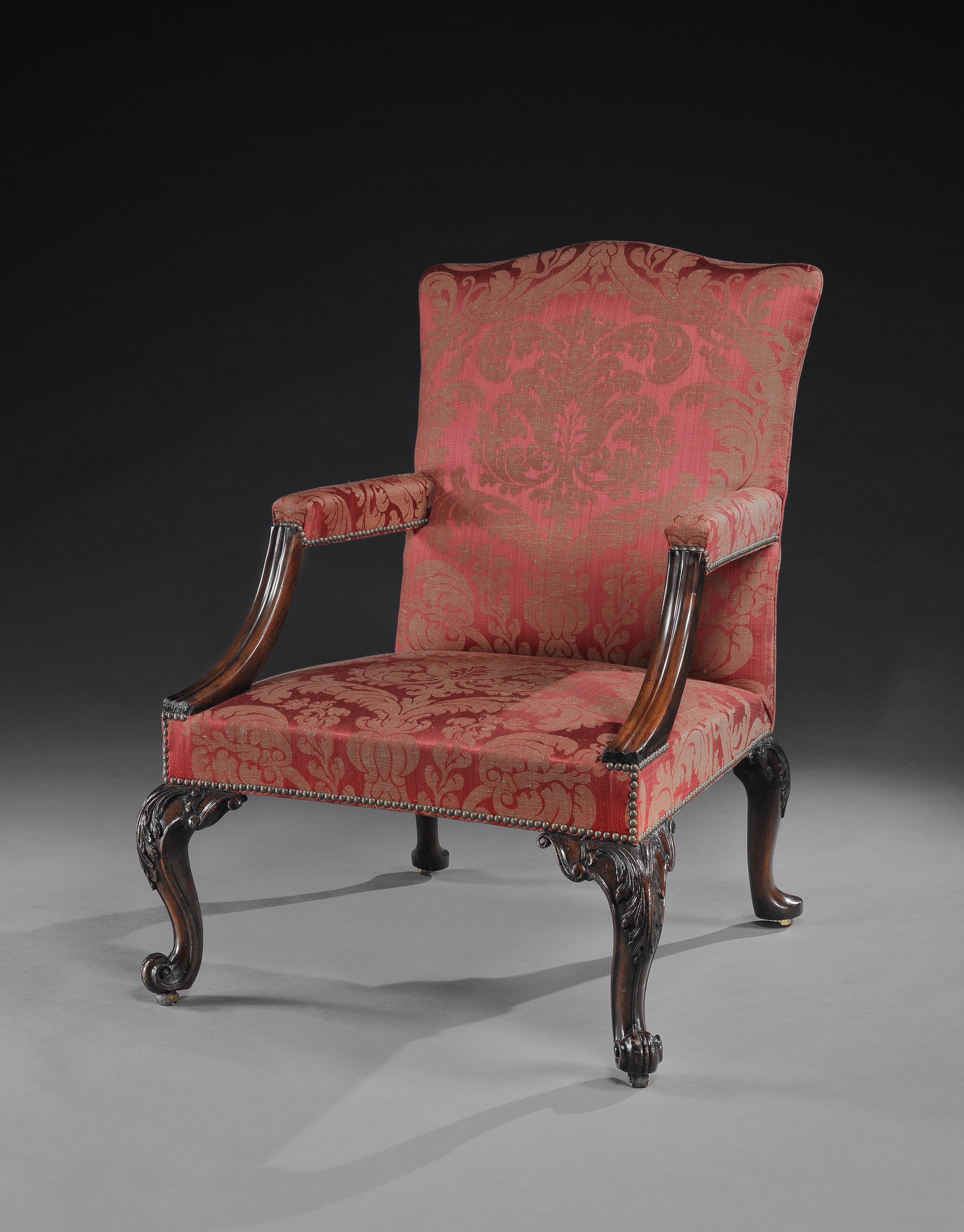 An extremely fine George II walnut library armchair of very generous proportions, with a serpentine shaped uphosltered back, the arm-rests ansd straight-fronted similarly upholstered, all  in a  brass-nailed damask, the walnut arm-supports slightly