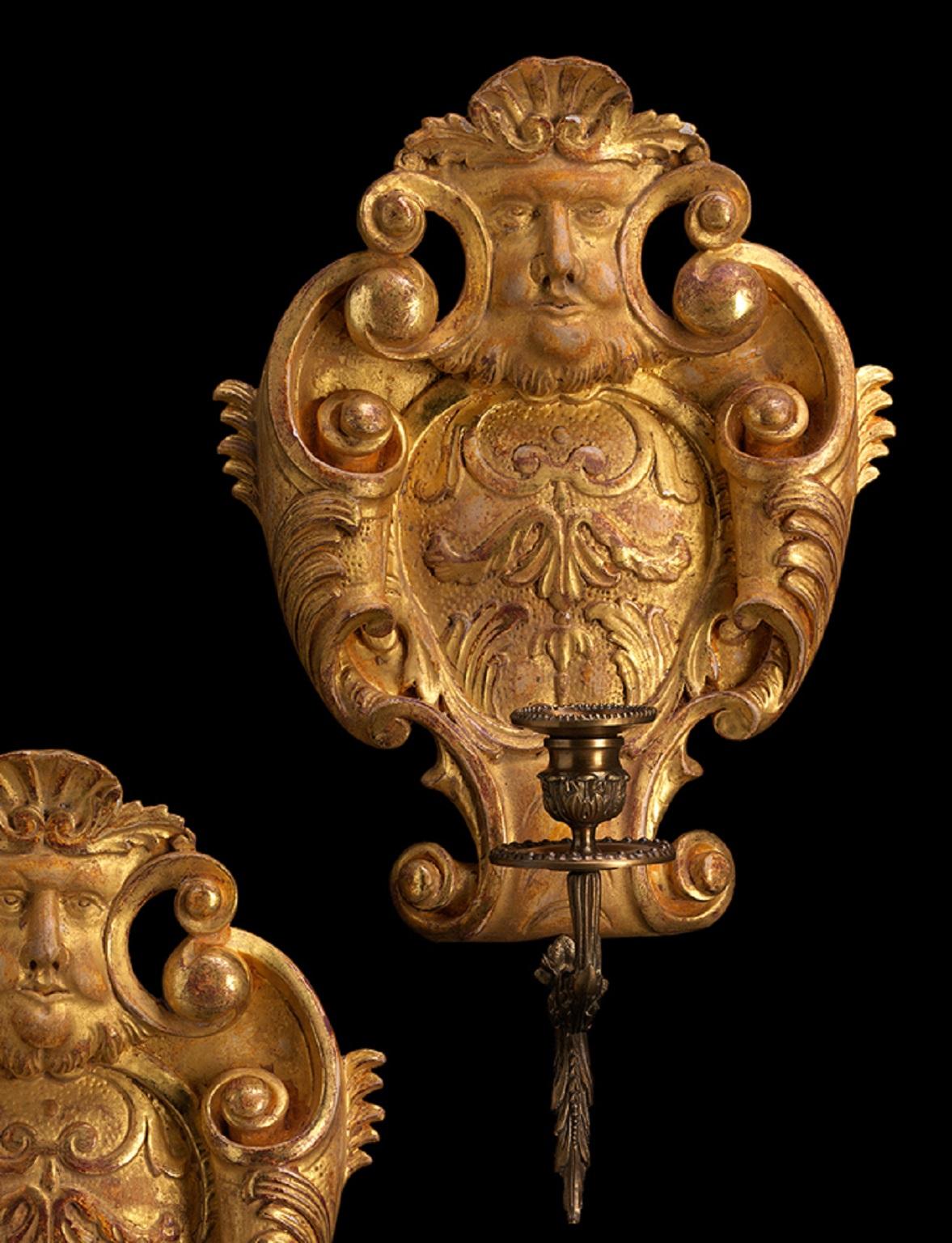 Este aplique de madera dorada tallada, al estilo de Jorge II y de la década de 1730, tiene forma de cartela. Dotado de un brazo de vela con volutas y hojas de acanto, está decorado con vigorosas volutas de hojas de acanto y un mascarón. Disponemos