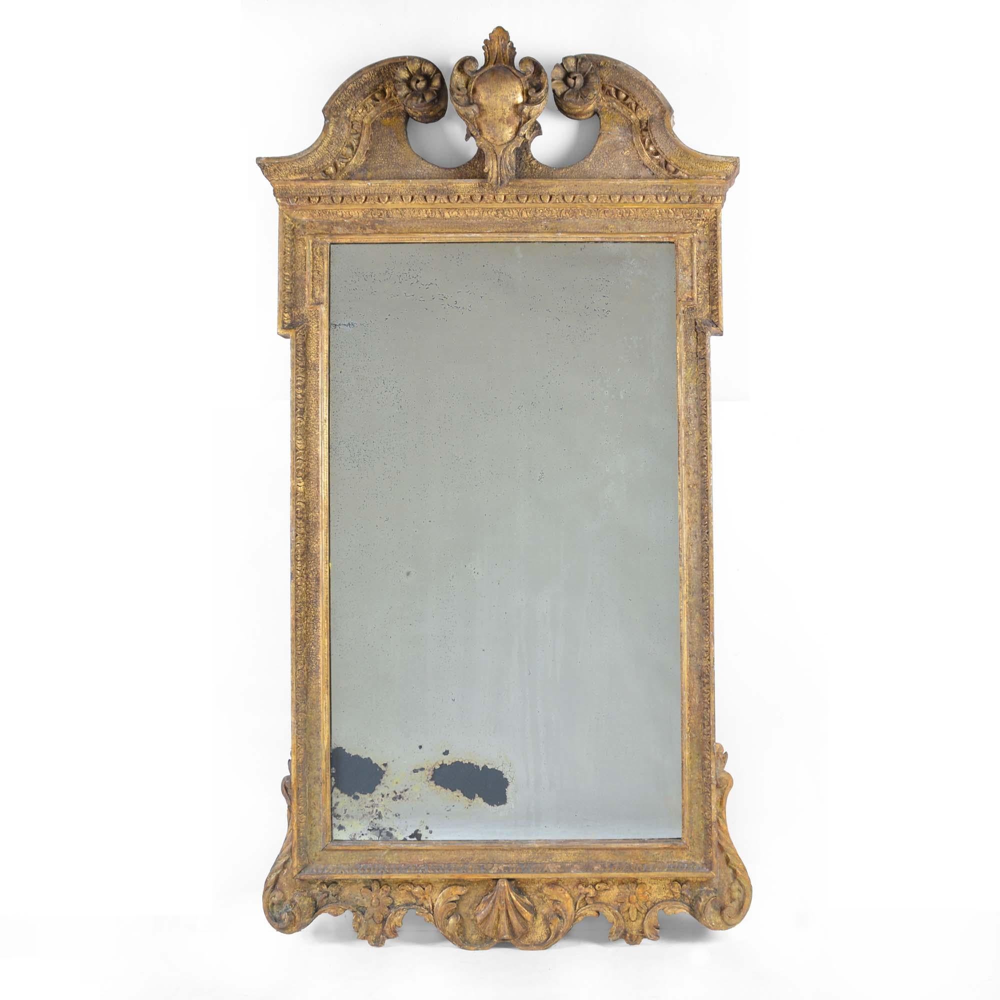 George II carved giltwood mirror with a broken swan-neck pediment centered by a cartouche, the frieze with egg and dart moulding. The original mirror plate with some foxing to the bottom, within a panelled and sanded surround, the apron with carved